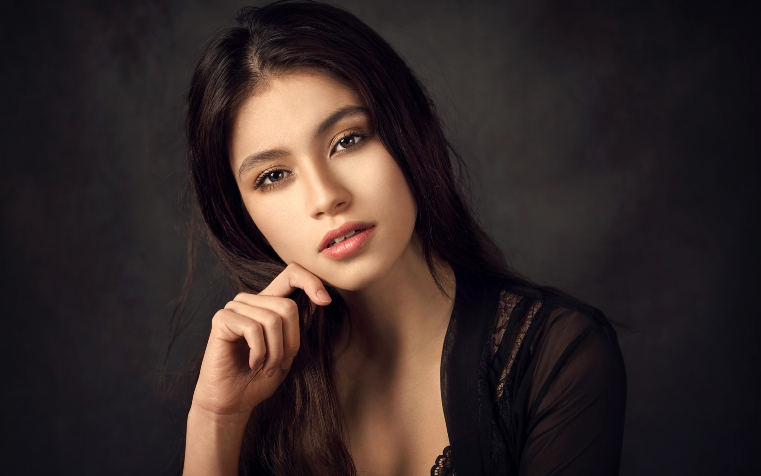 Красивая девушка в черном сидит на сером фоне