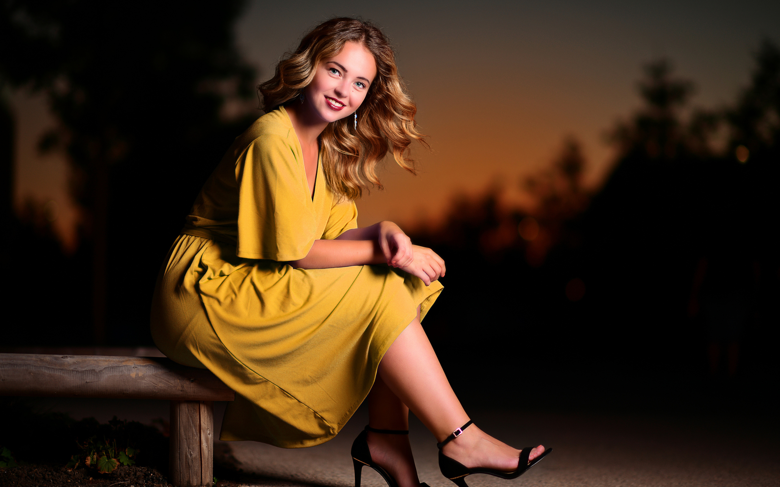 Красивая улыбающаяся девушка в желтом платье сидит на лавке 