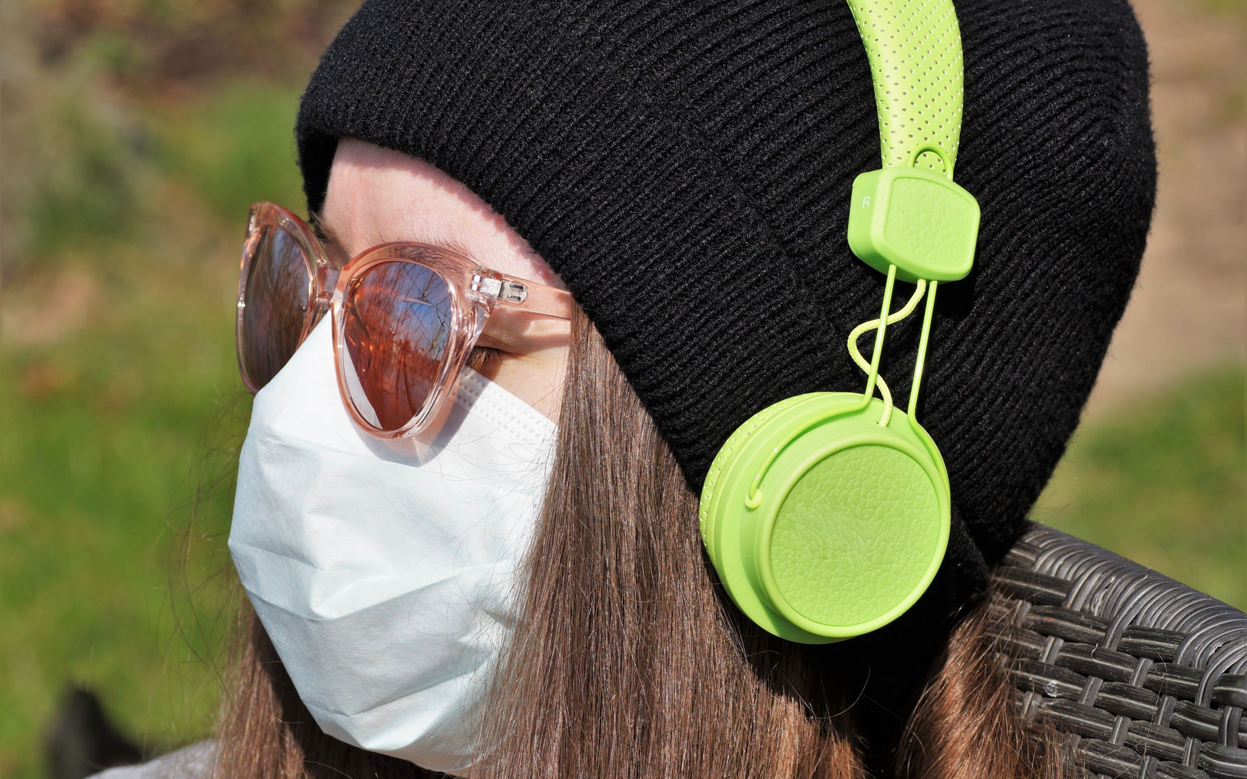 Девушка в медицинской маске на лице, в черной маске и наушниках