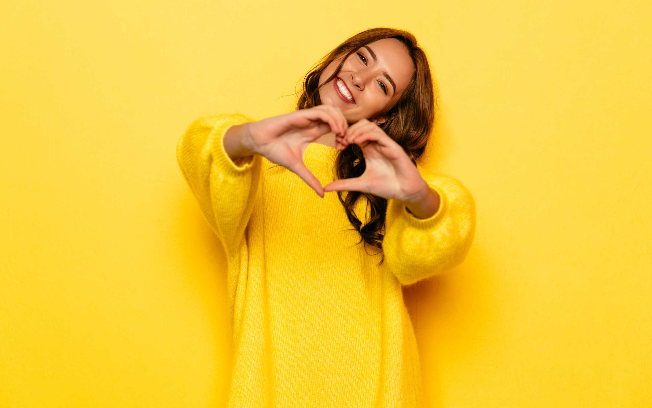 Девушка в желтом свитере показывает сердце руками