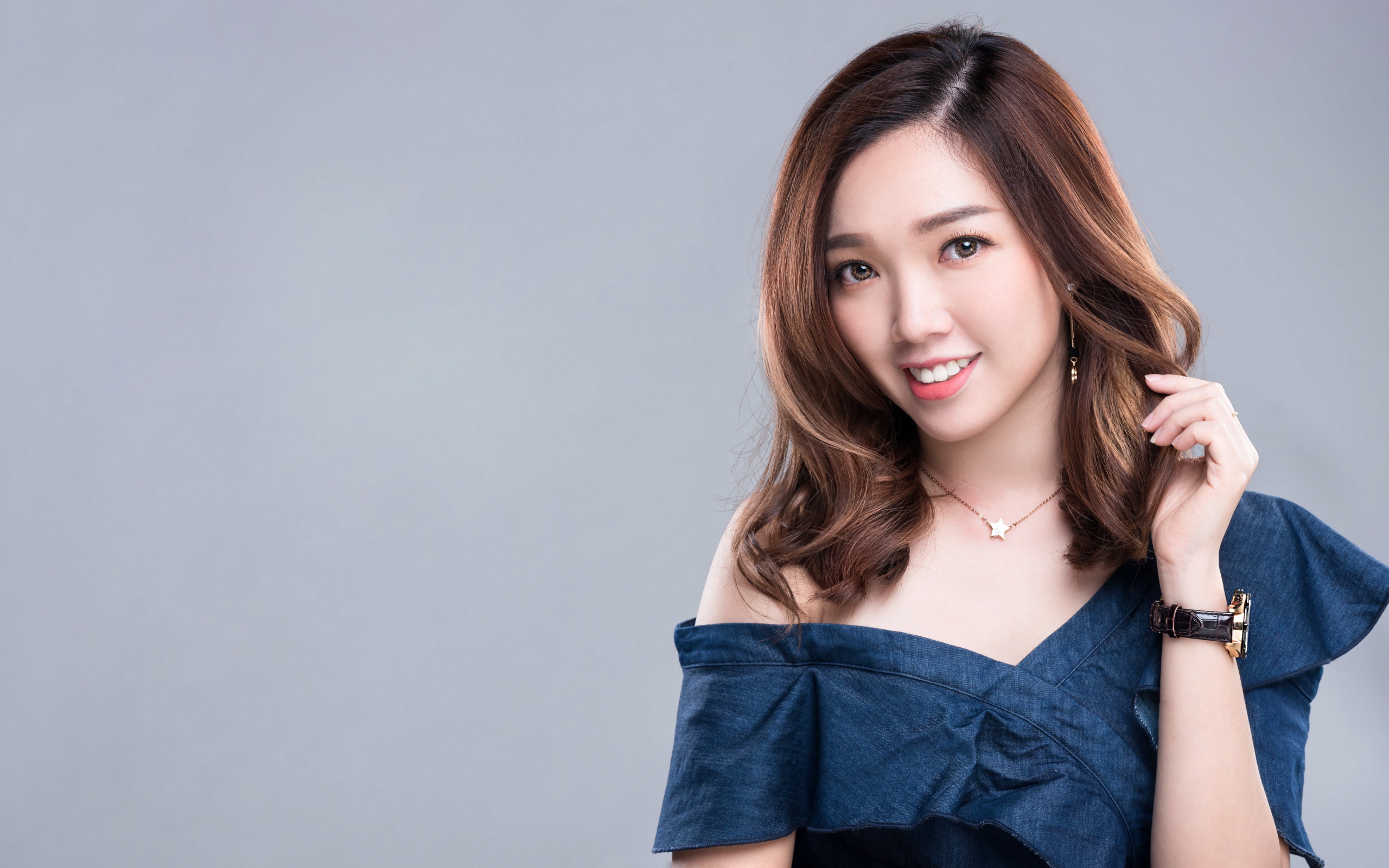 Улыбающаяся девушка азиатка с часами на руке на сером фоне