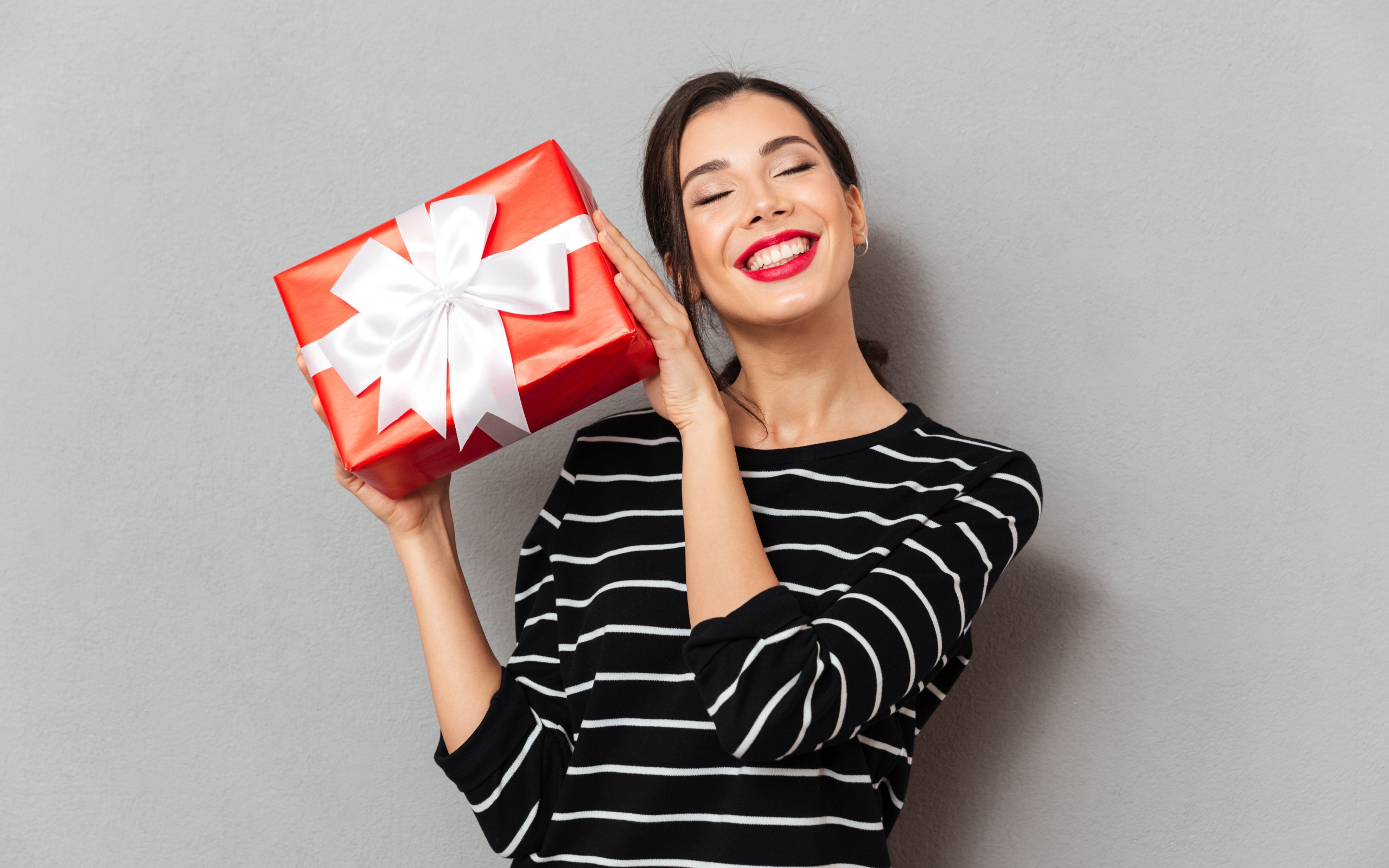 Улыбающаяся девушка с подарком в руках на сером фоне 