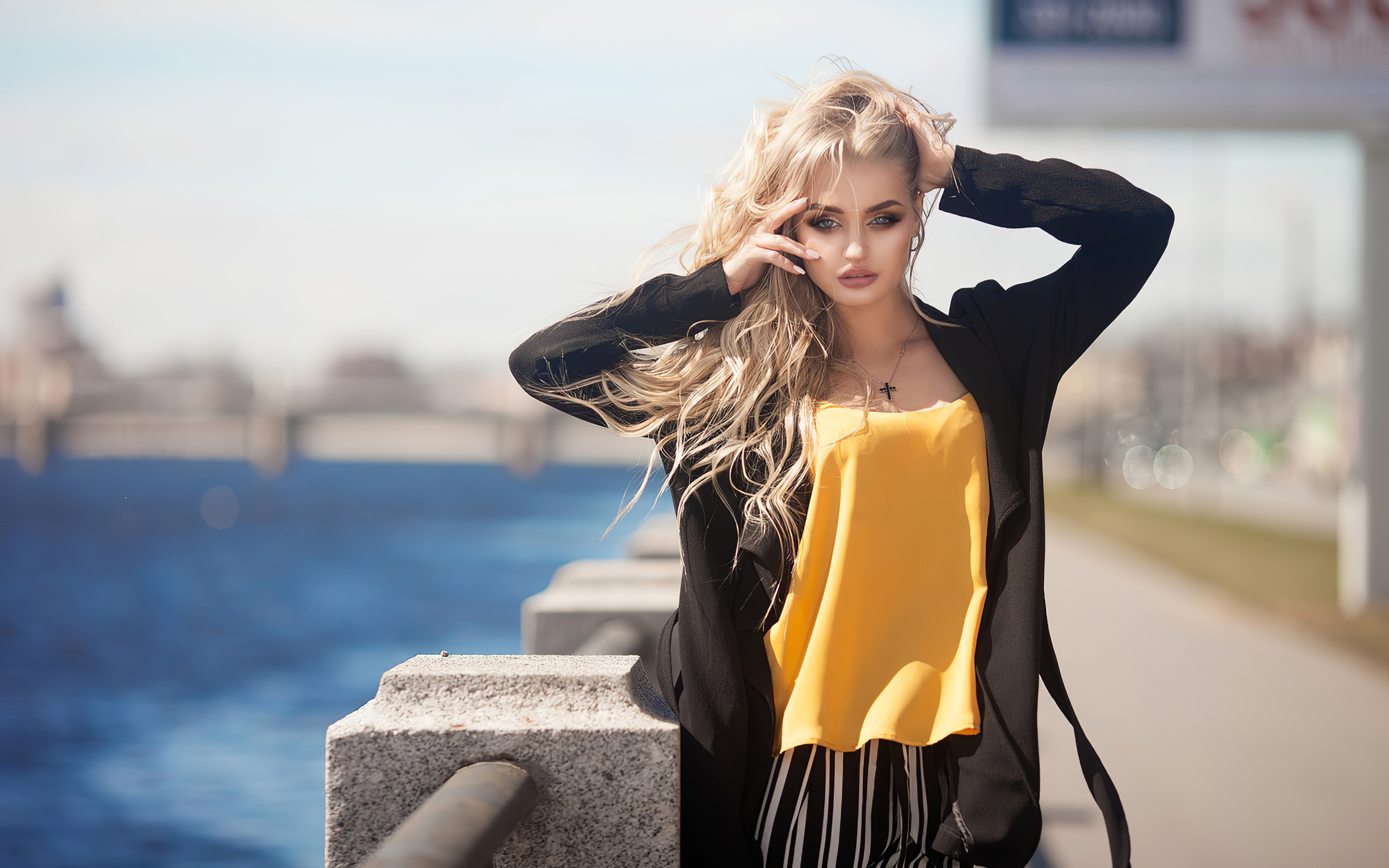 Эффектная блондинка в черном пальто стоит у воды