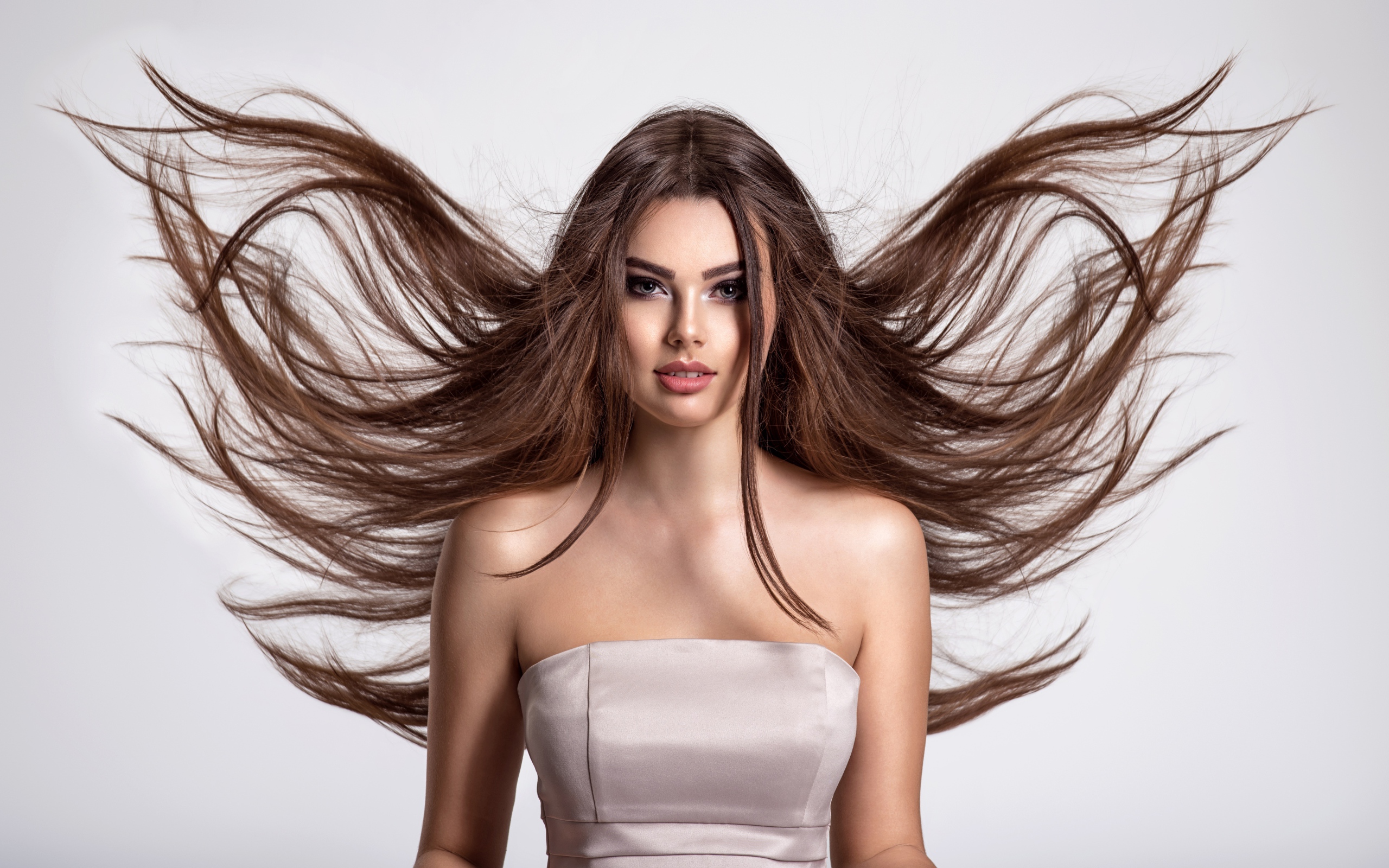 Ветер развивает волосы красивой девушке шатенке на сером фоне