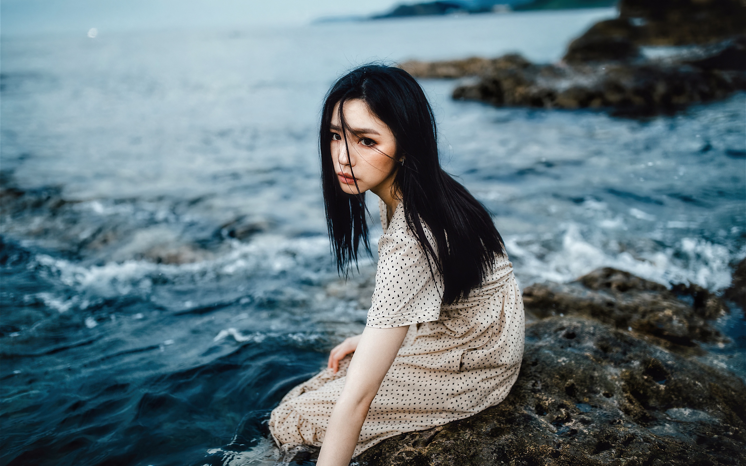 Молодая девушка азиатка сидит на камне у воды