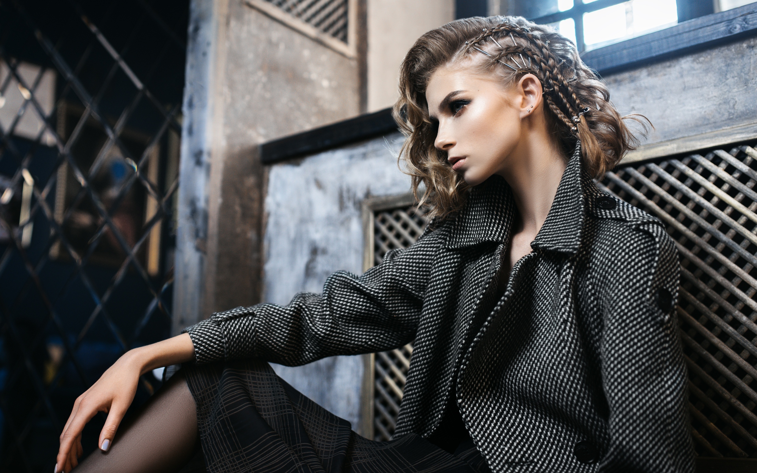 Молодая девушка в сером пальто сидит у стены