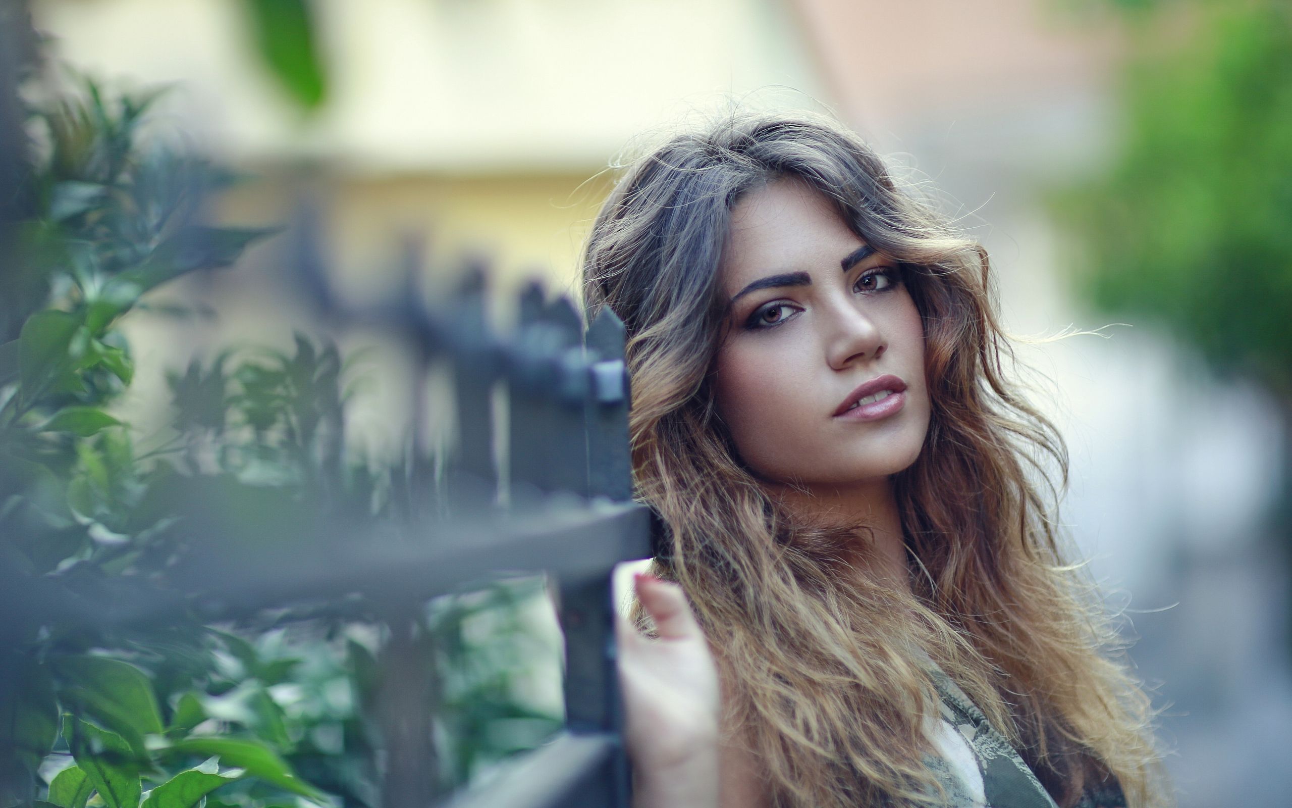 Молодая девушка с длинными волосами стоит у забора