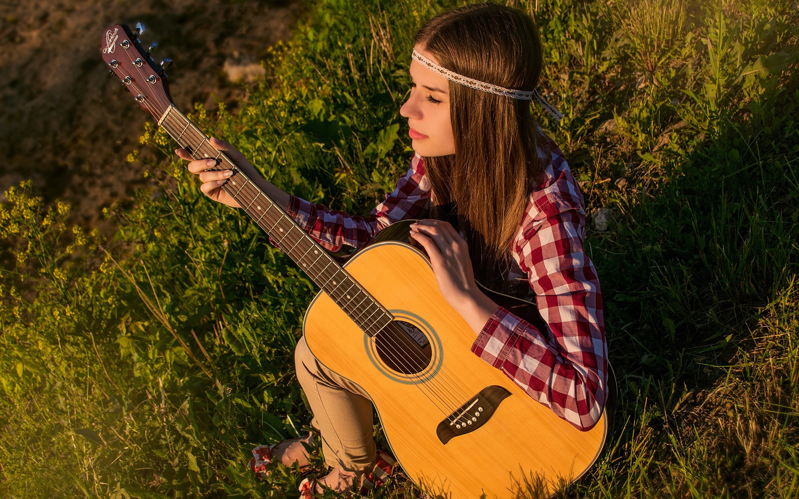 Молодая девушка хиппи сидит с гитарой на траве 