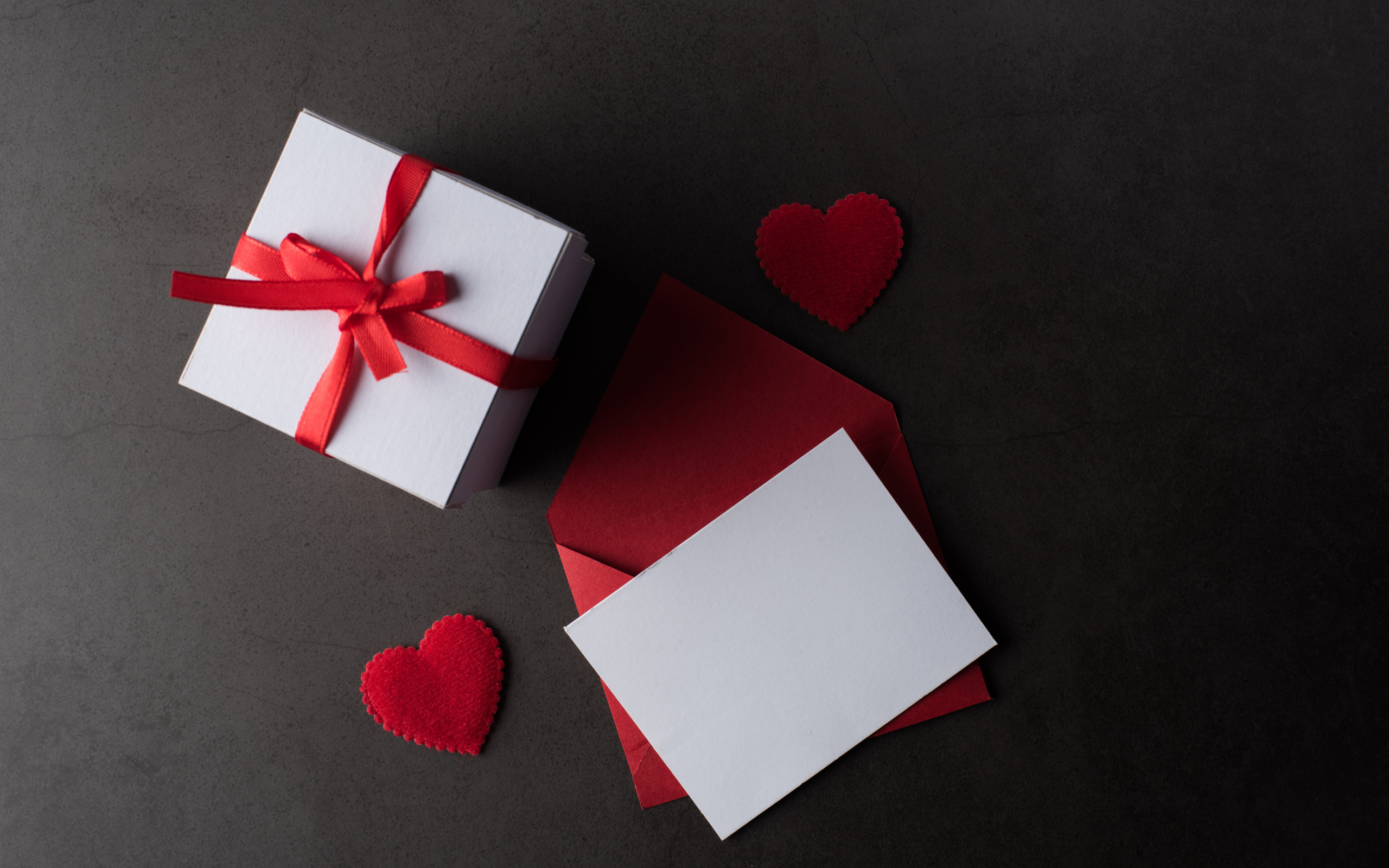 Envelope and gift on a gray table with red hearts.