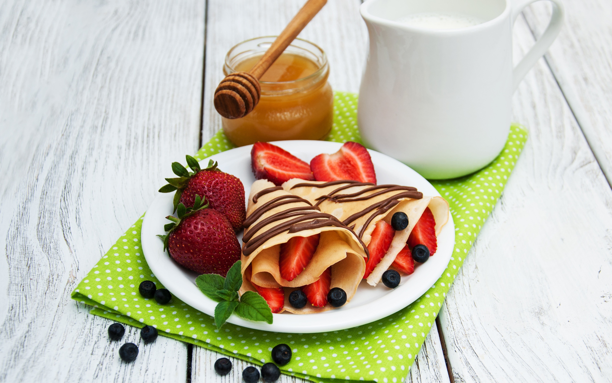 Вкусные блины с клубникой на столе с молоком и медом на праздник Масленица