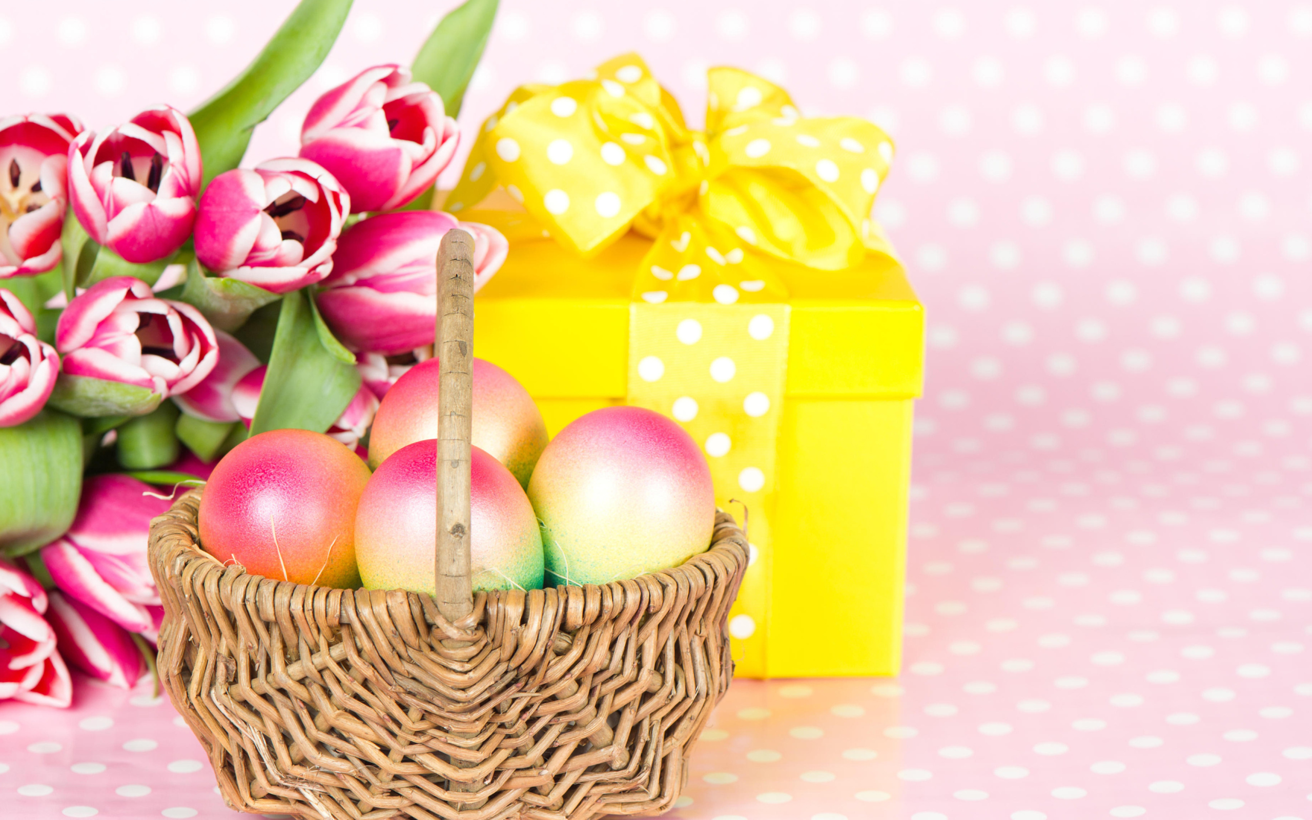 Корзина с пасхальными яйцами на столе с подарком и букетом тюльпанов 