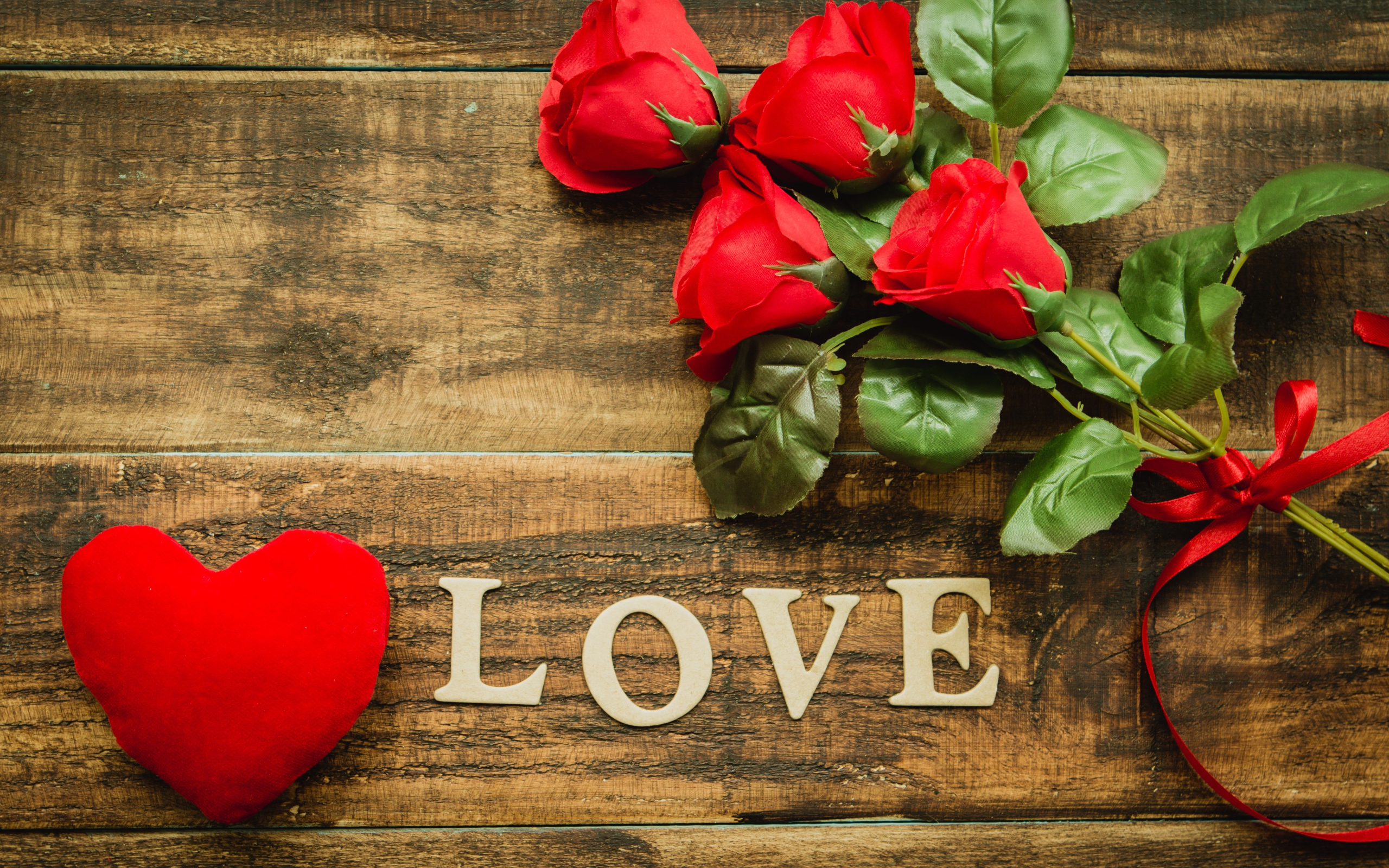 Надпись LOVE на столе с розами и красным сердцем