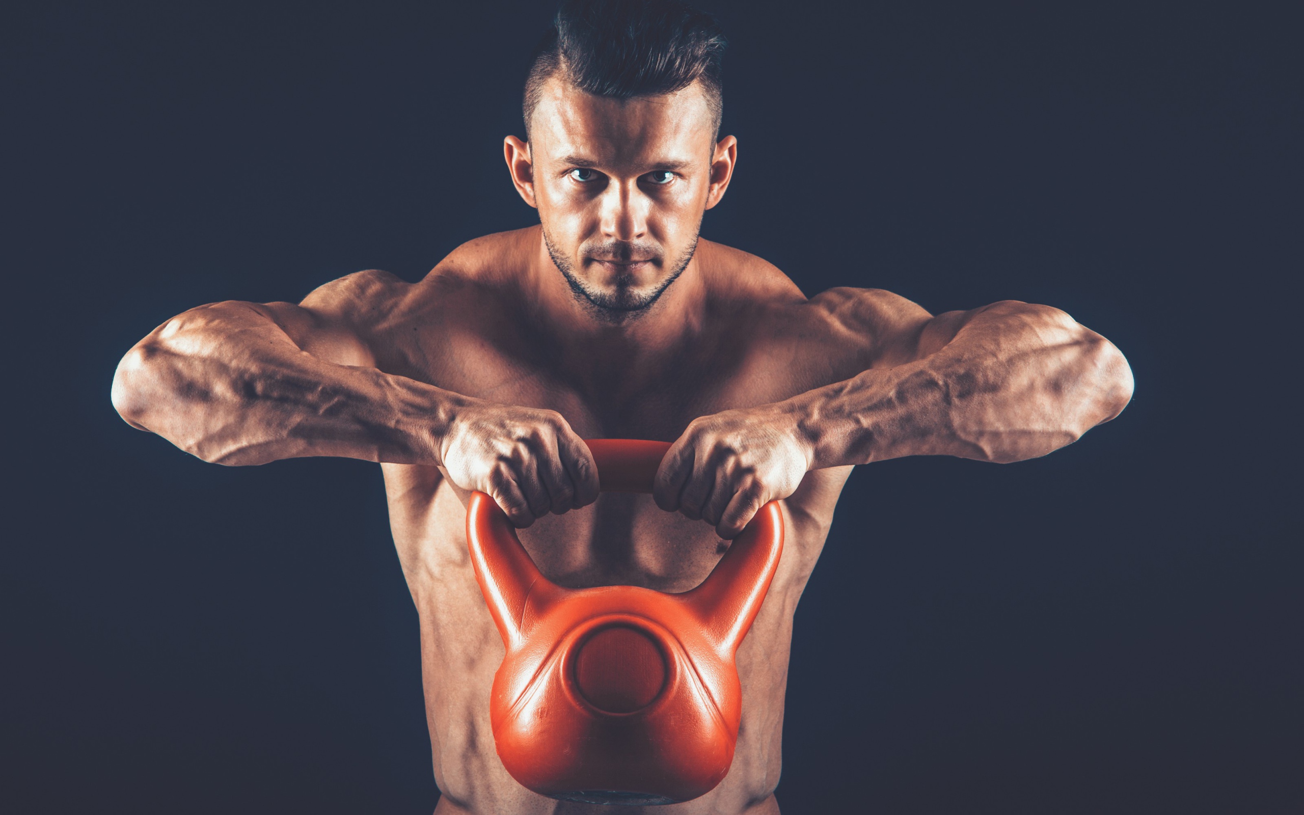 Накаченный парень поднимает тяжелую гирю на черном фоне