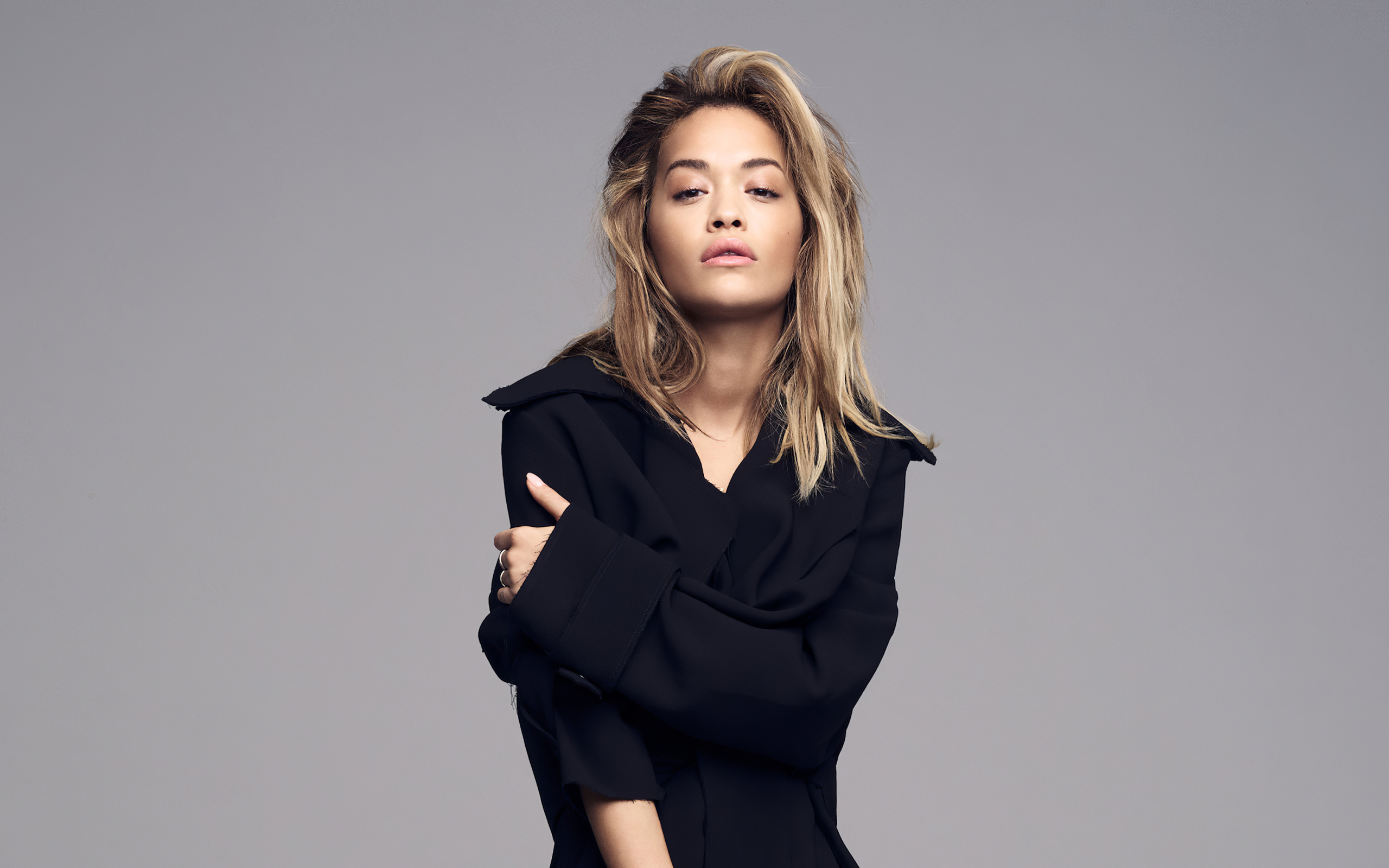 Певица Рита Ора в черном наряде на сером фоне