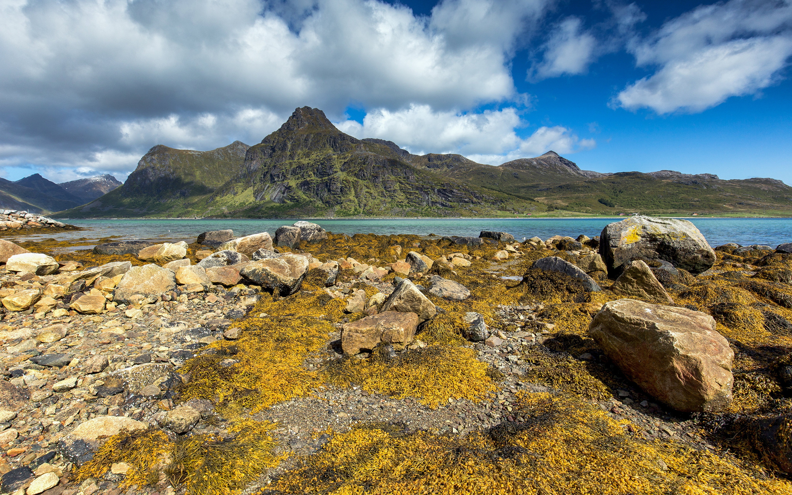 Камни на берегу реки под белыми облаками в голубом небе 