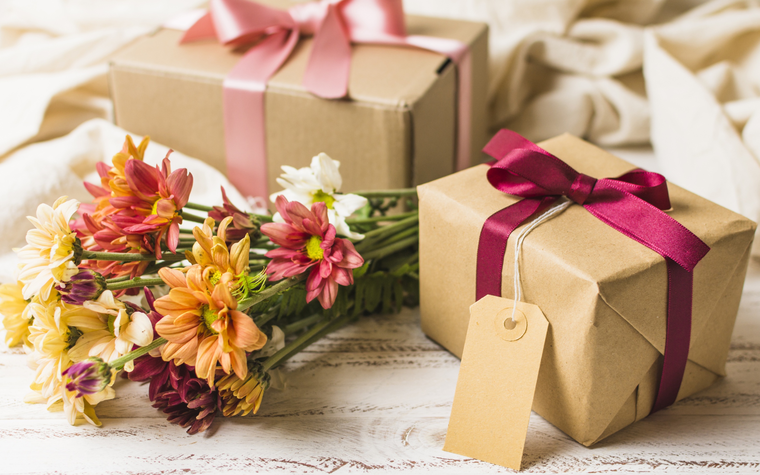 Букет разноцветных хризантем с подарками на столе 