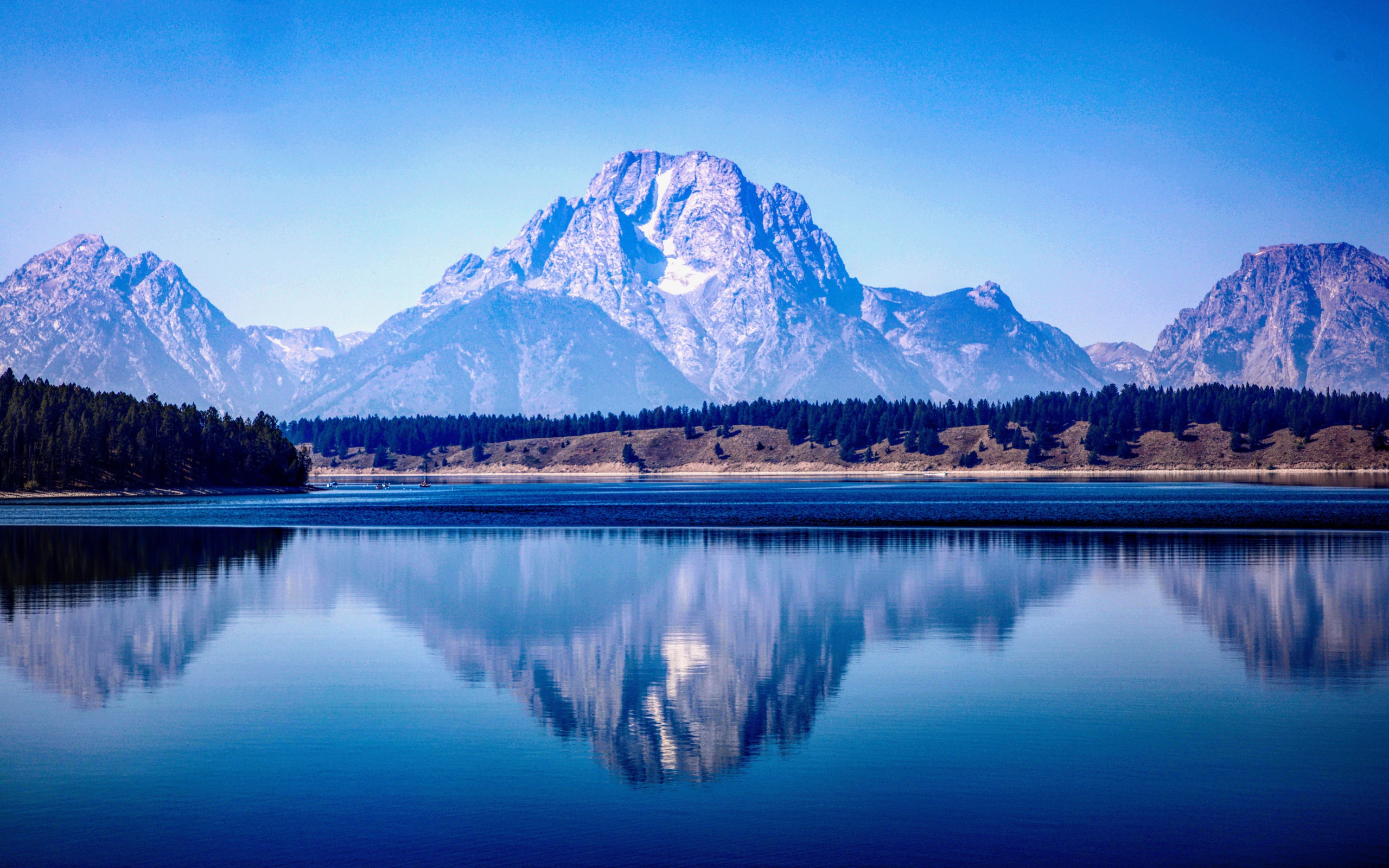 High mountains are reflected in a lake under a blue sky