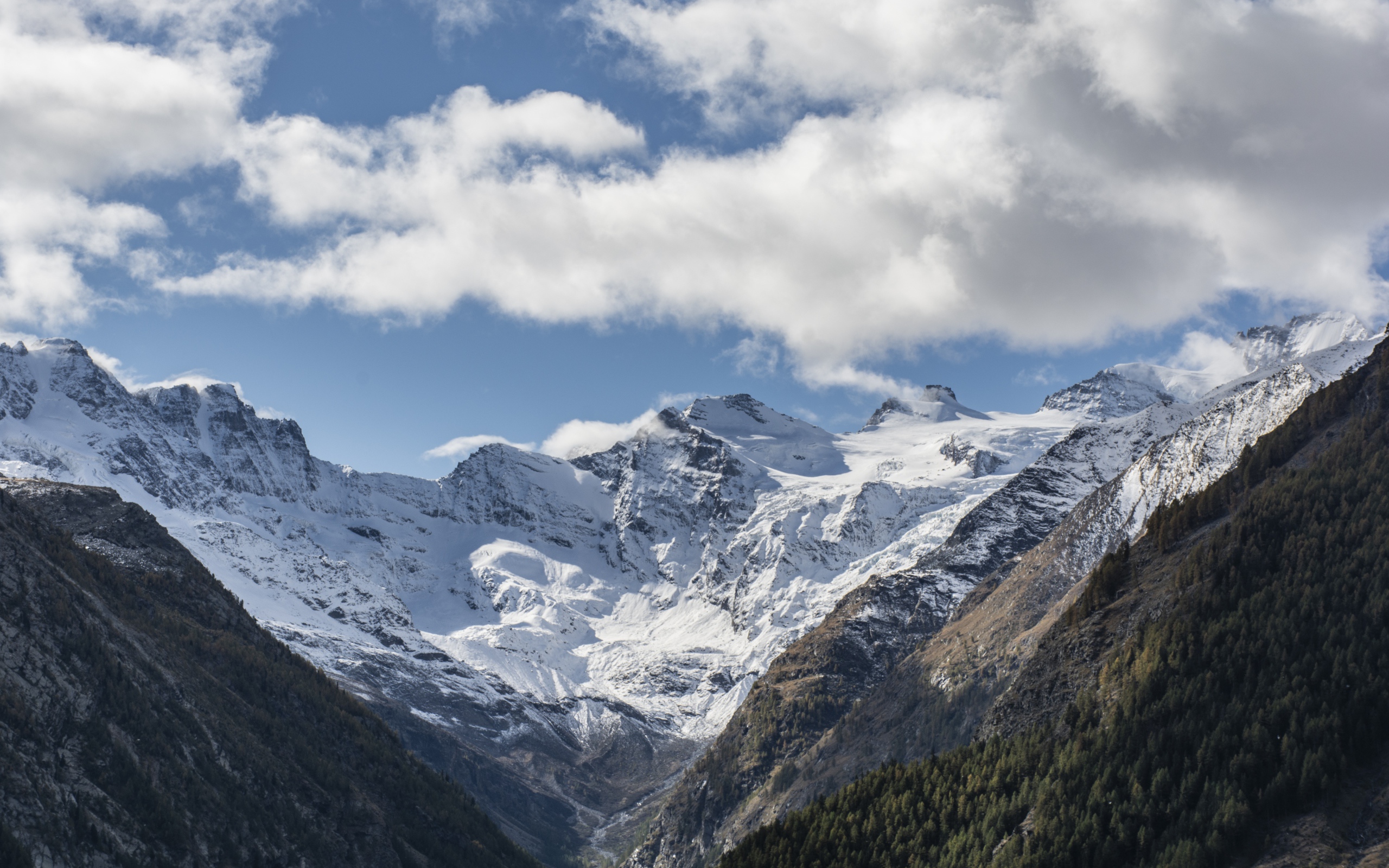 Заснеженные горы под голубым небом с белыми облаками