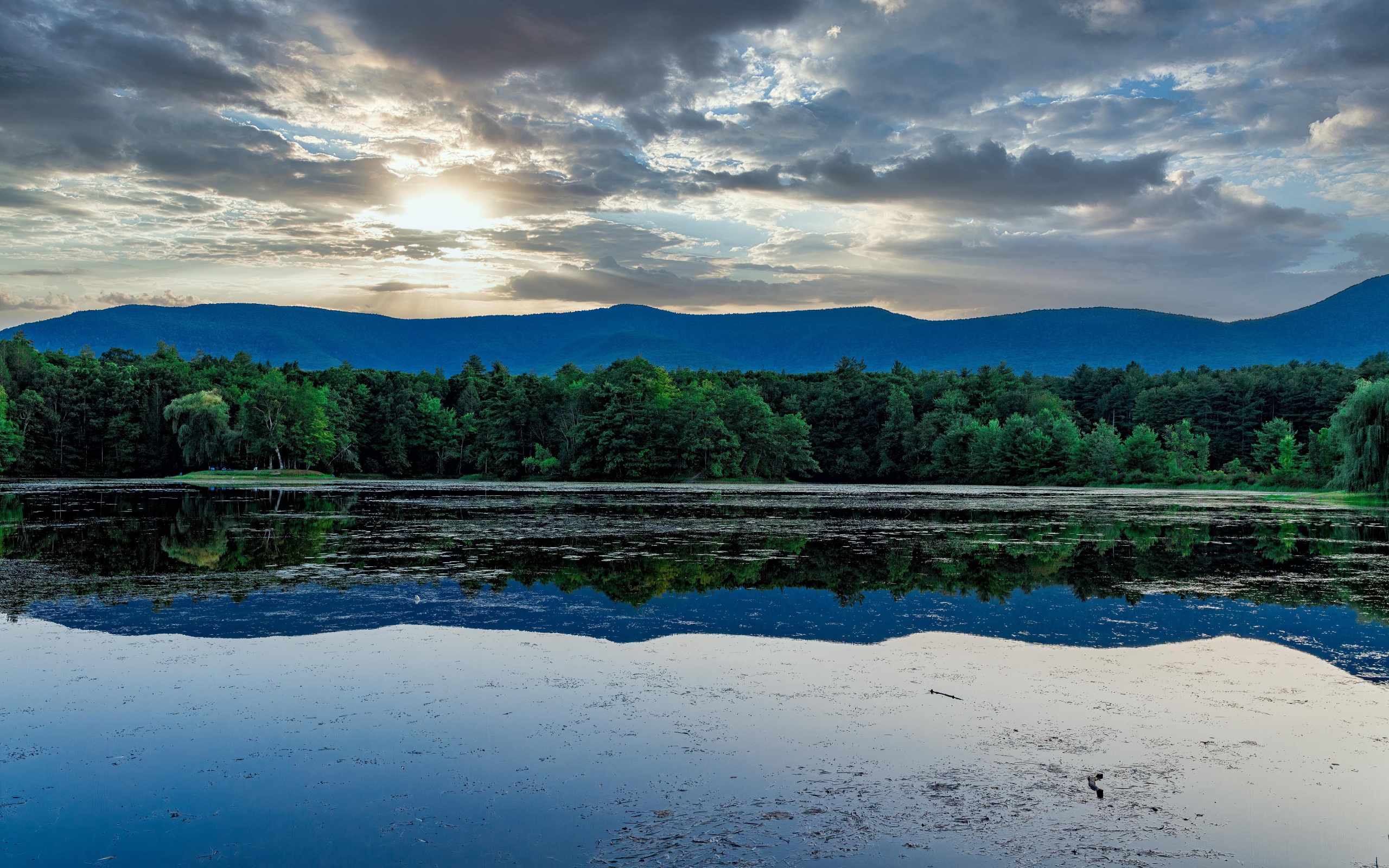 Солнце пробивается сквозь облака в небе над озером