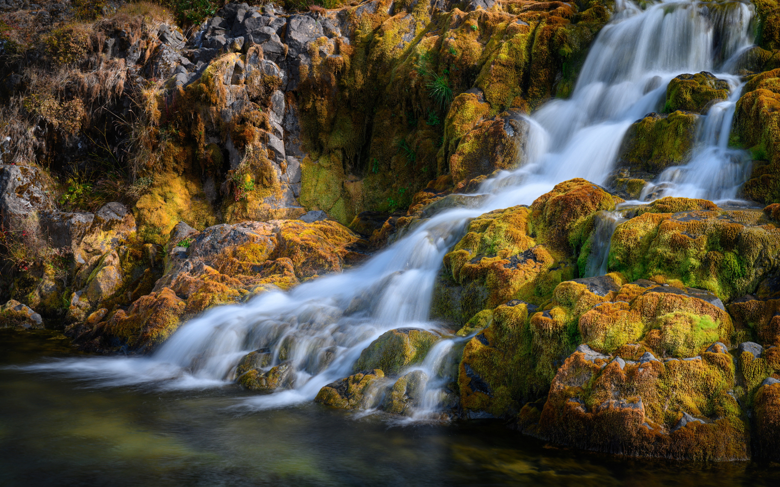 Быстрая вода водопада стекает по покрытым мхом камням, Исландия 