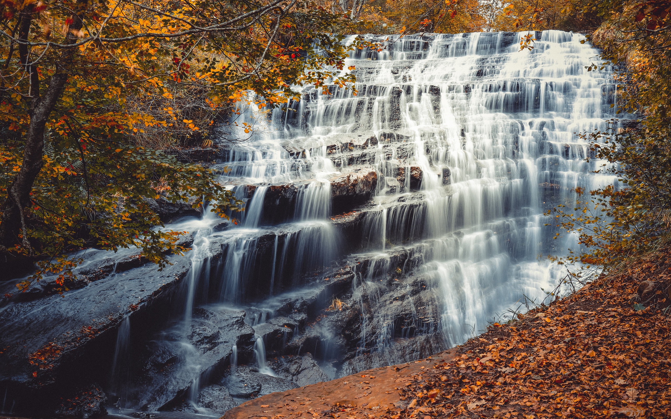 Быстрая вода водопада стекает по каскадам камней осенью