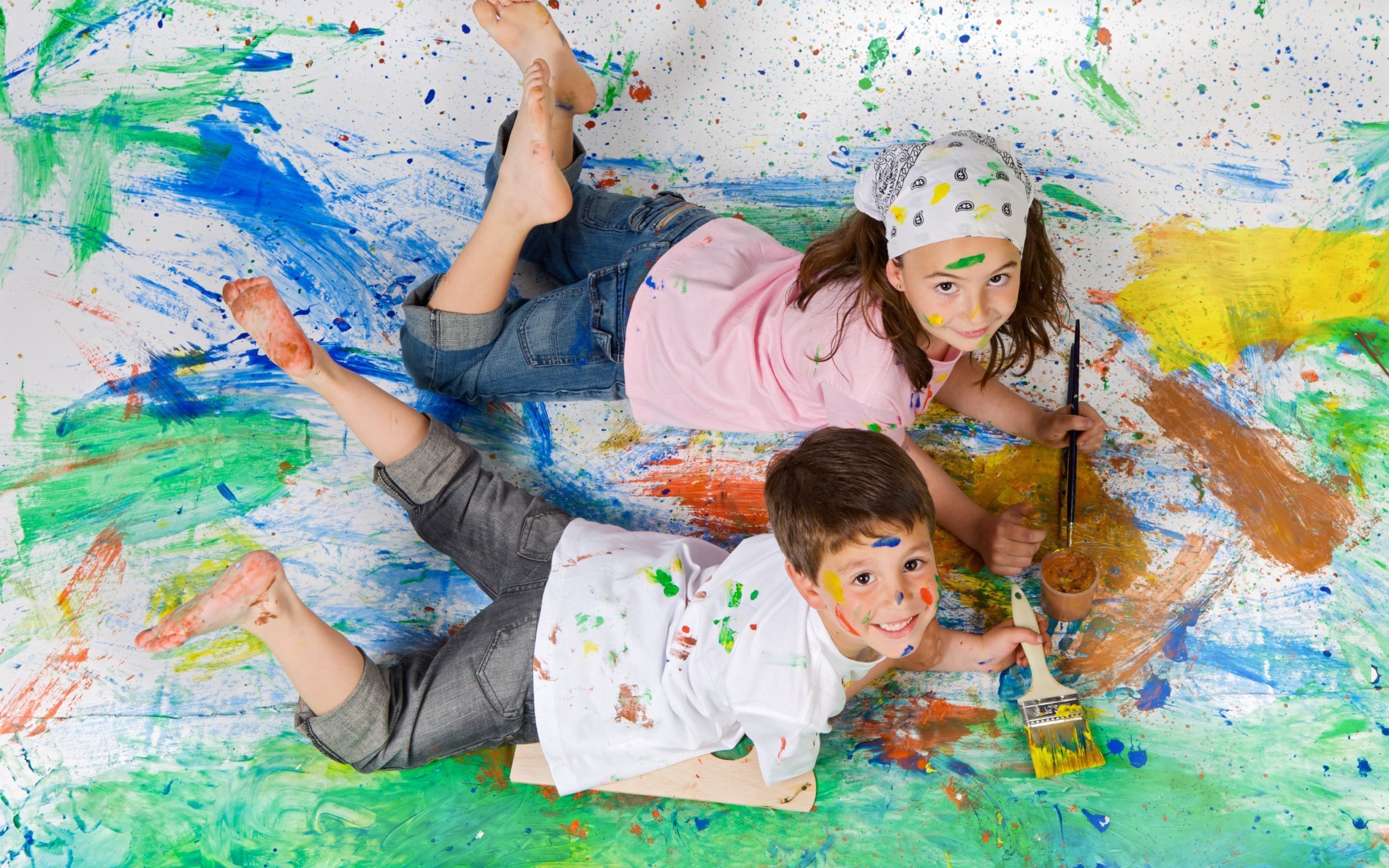 Маленькие мальчик и девочка рисуют красками на полу 