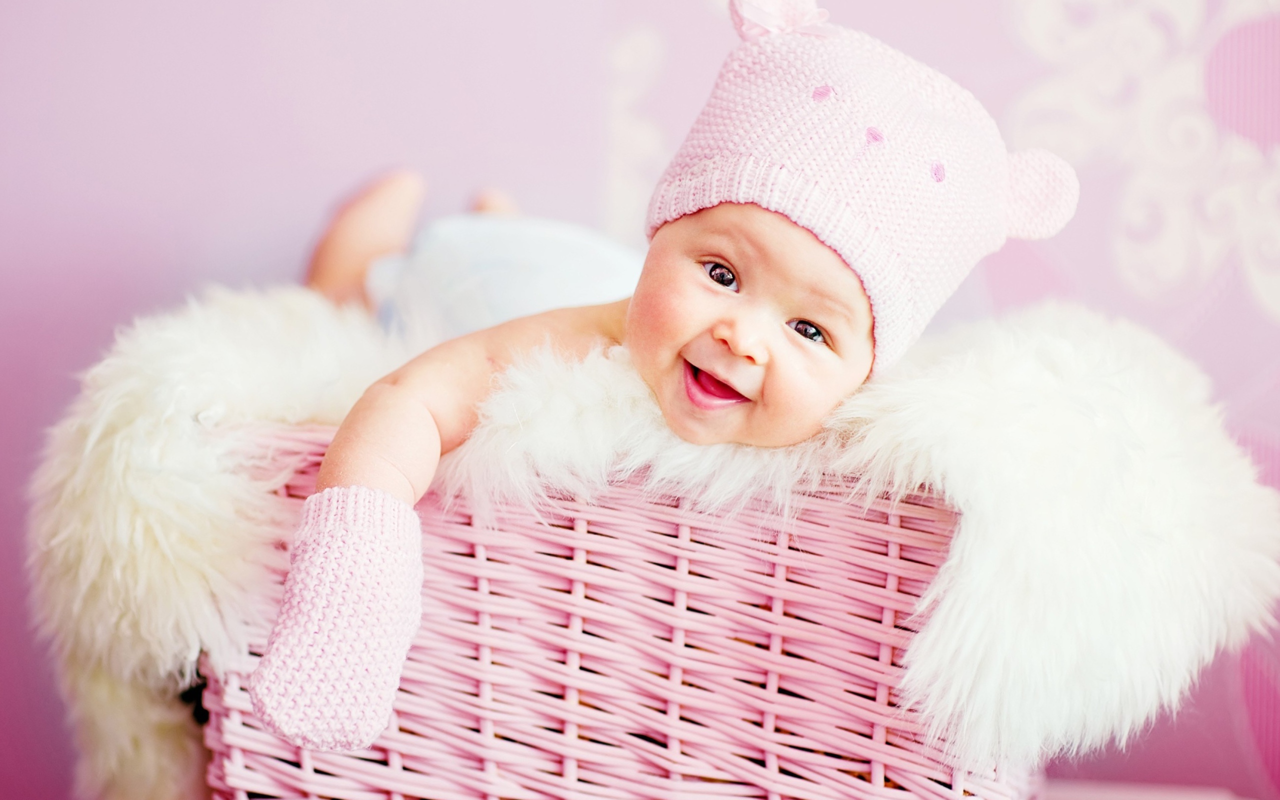 Улыбающийся грудной ребенок в шапке в розовой корзине 