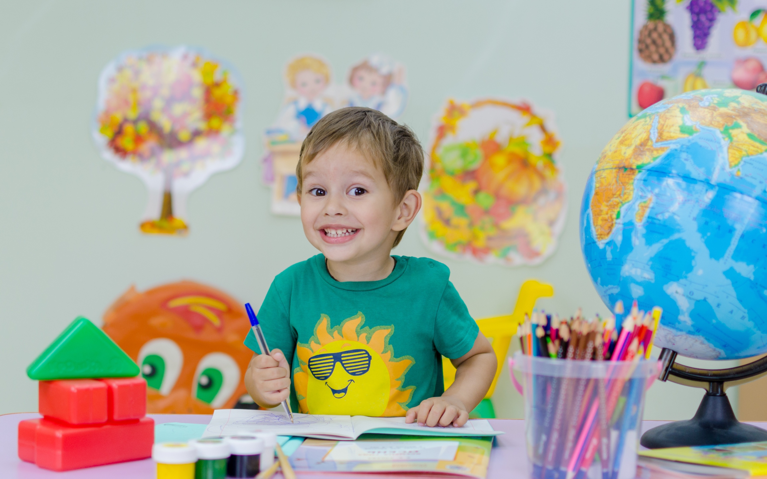 Улыбающийся мальчик школьник с канцелярскими предметами на столе 