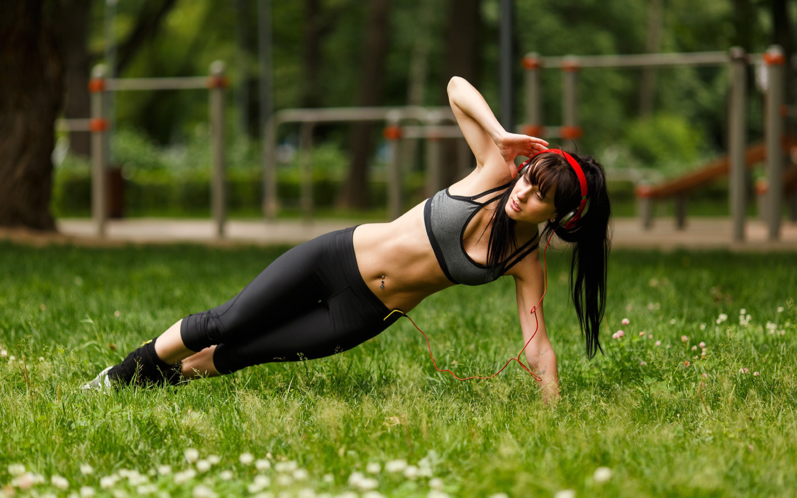 Девушка с наушниками на голове занимается фитнесом на траве 