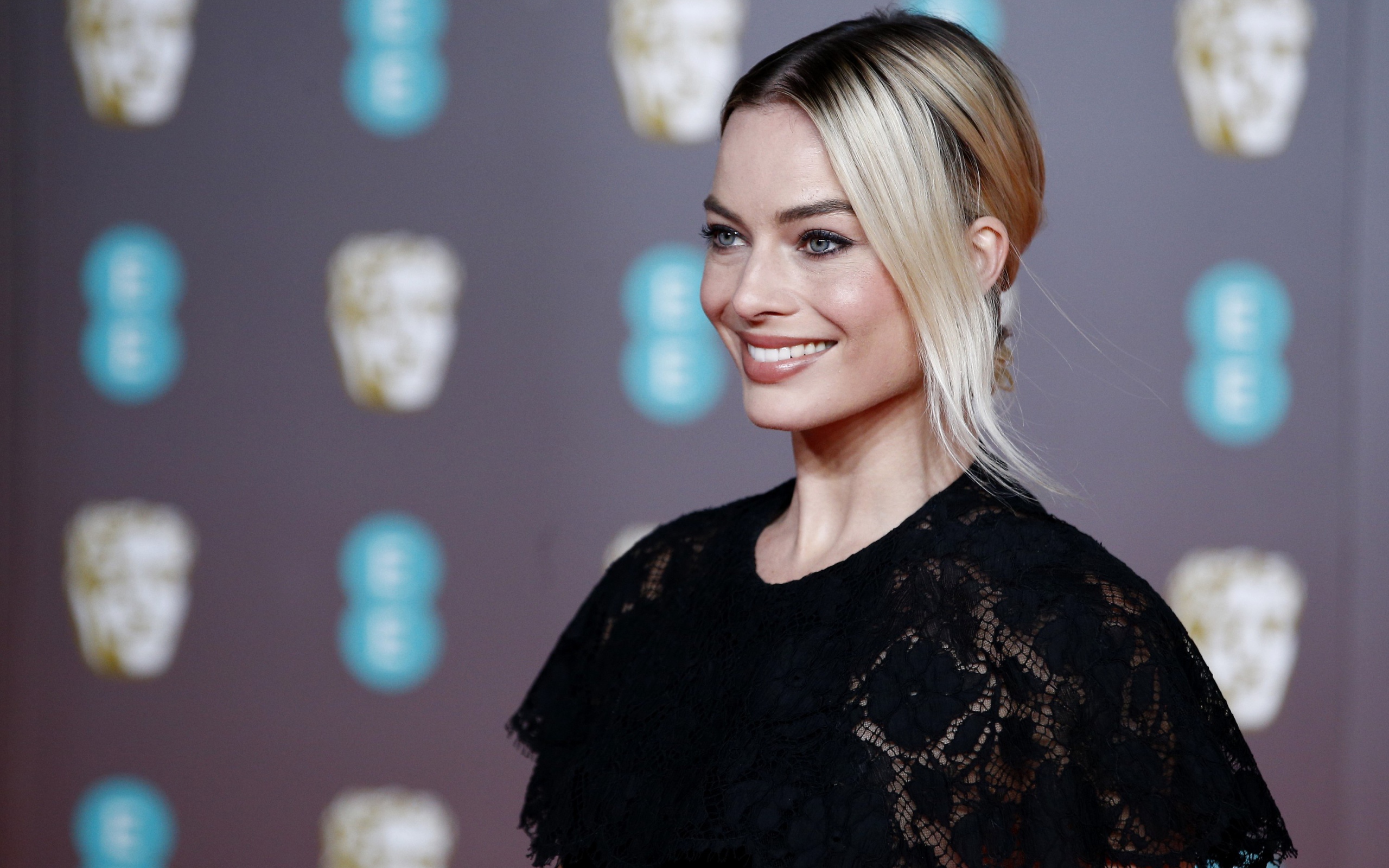 Улыбающаяся актриса Марго Робби в черном платье 