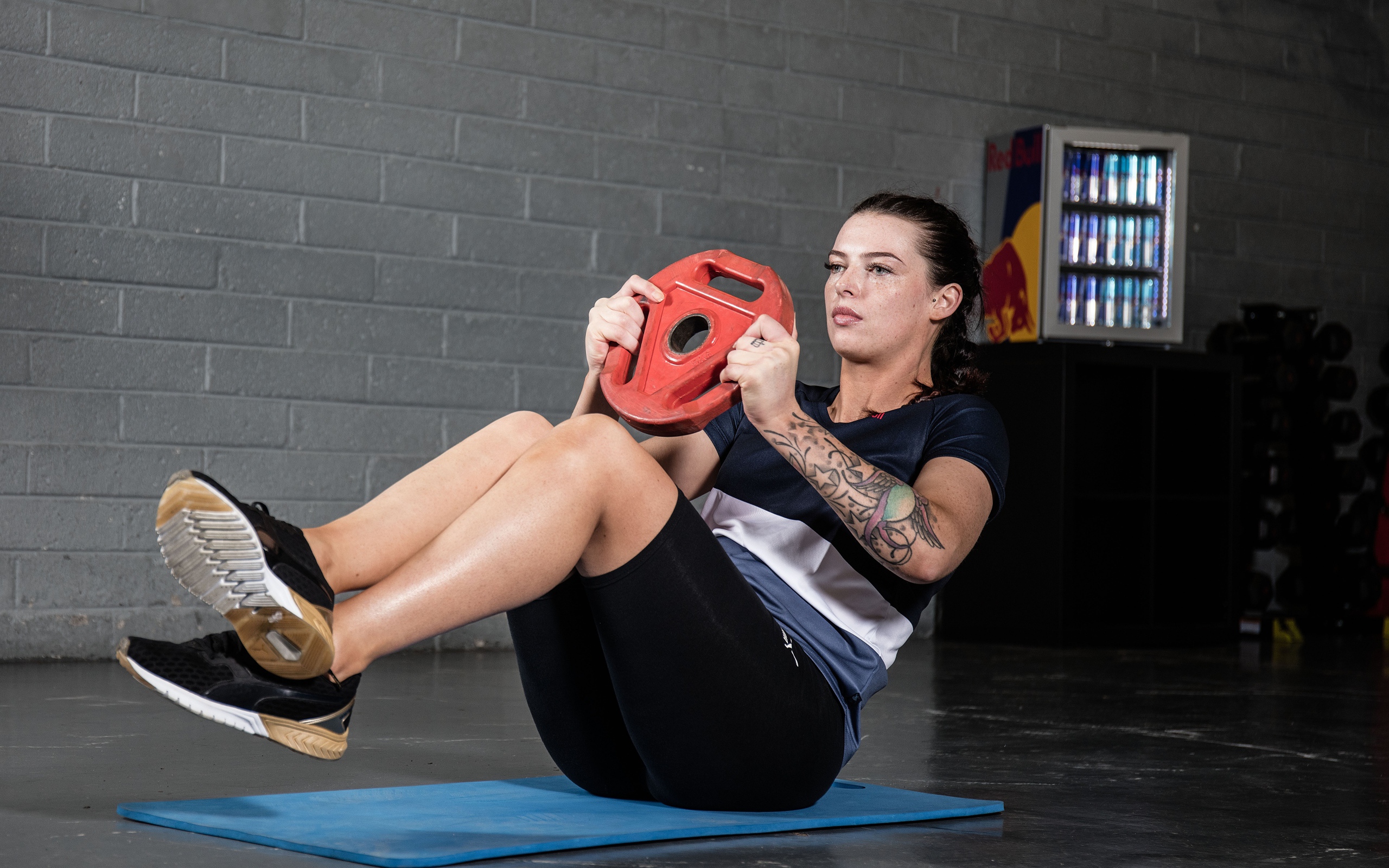 Сильная девушка с татуировками на руке качает пресс 