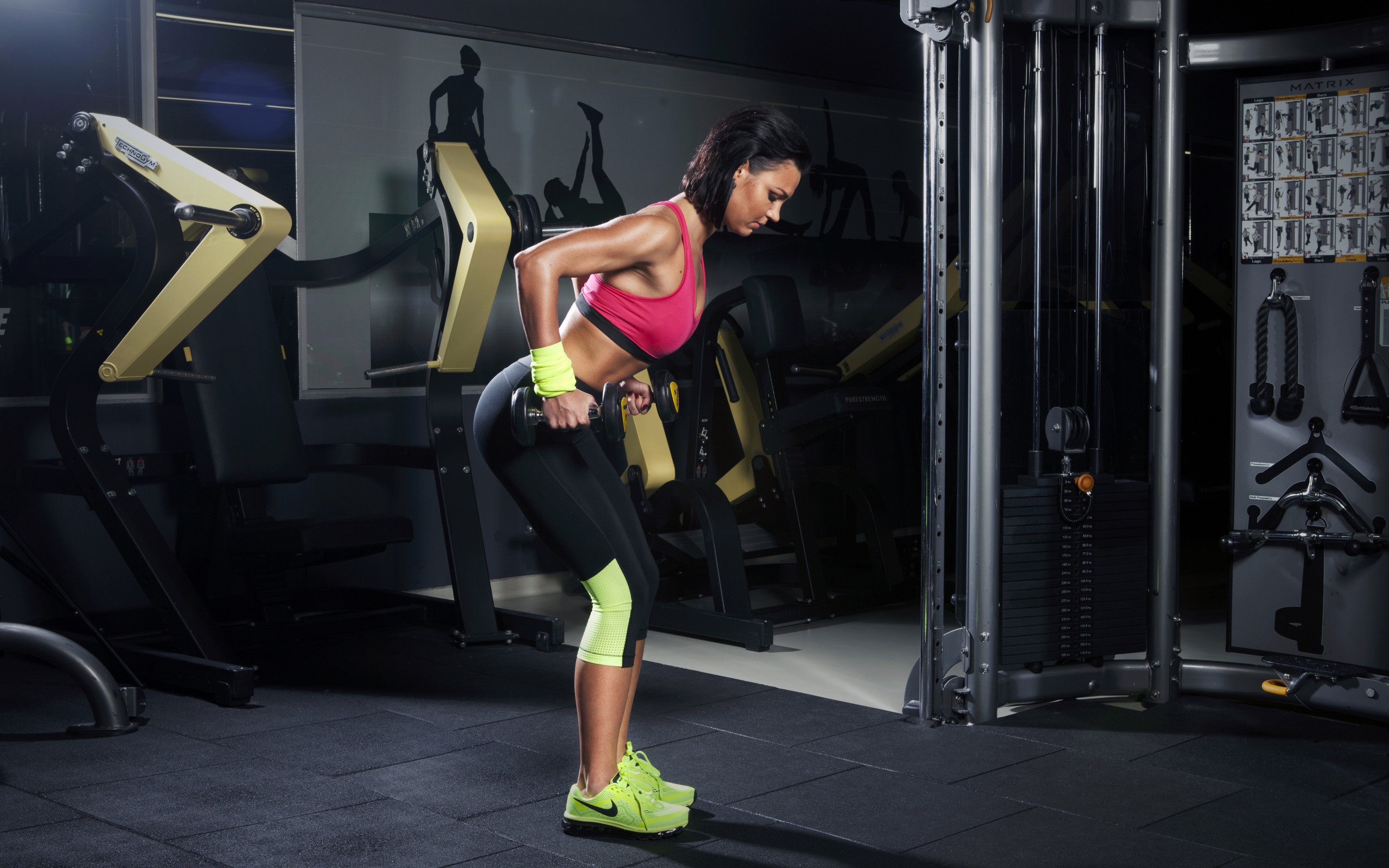 Девушка занимается с гантелями в спортзале у тренажеров 