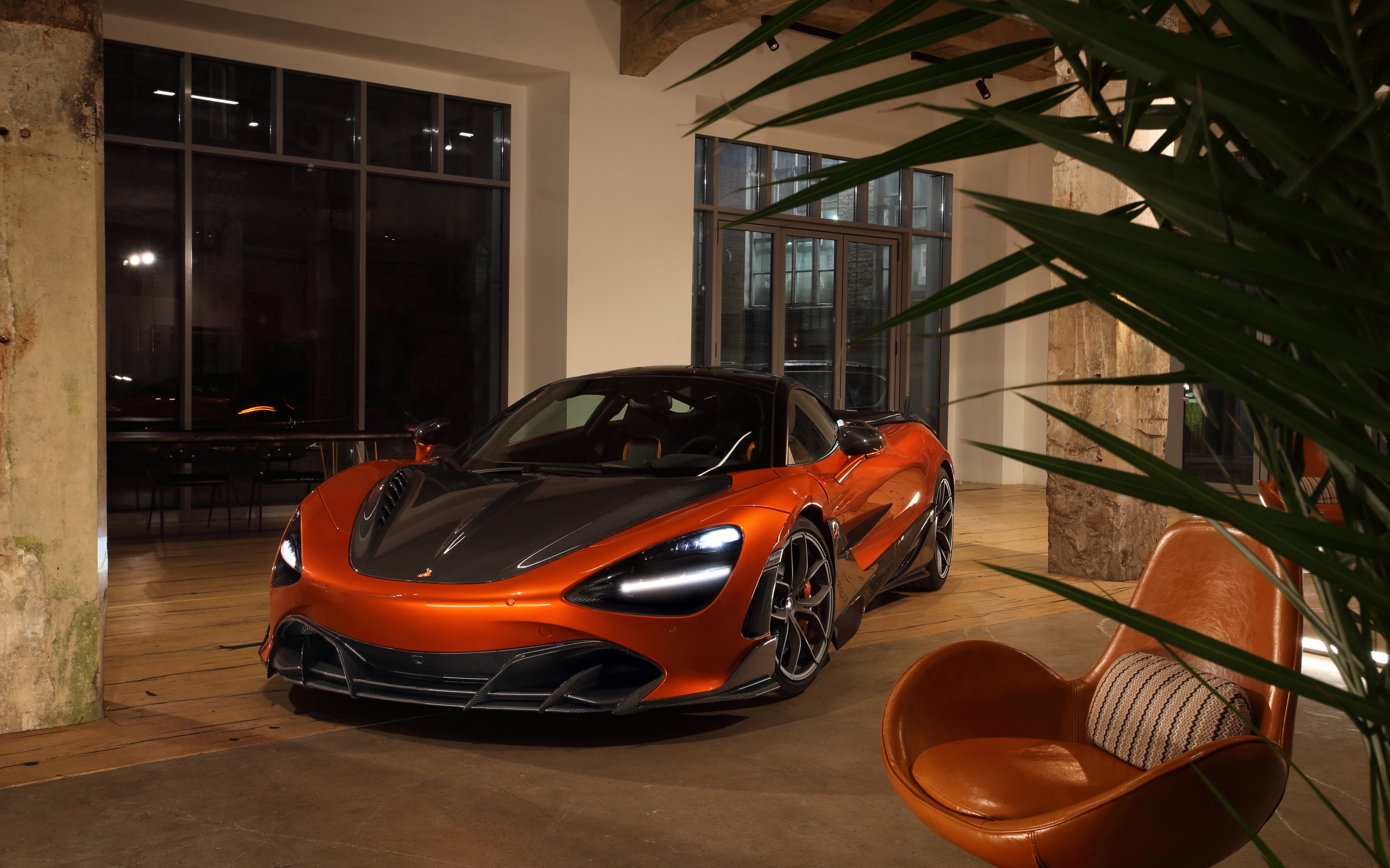 Оранжевый автомобиль  McLaren 720S у дома с креслом
