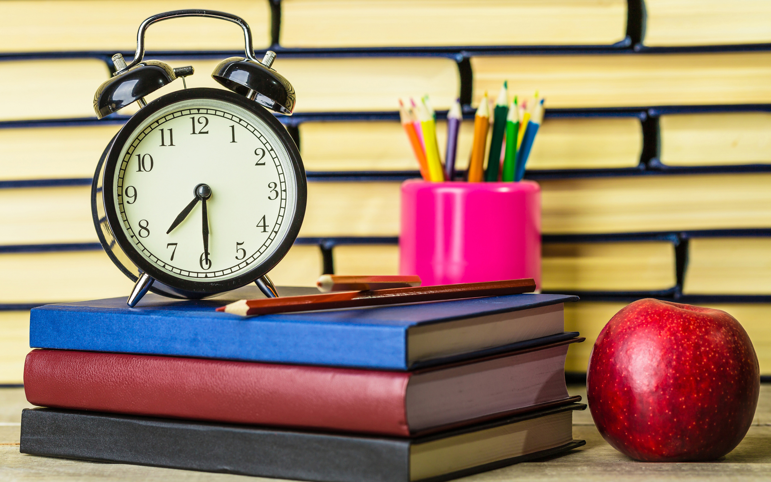 Будильник, книги, карандаши и яблоко на столе у стены 