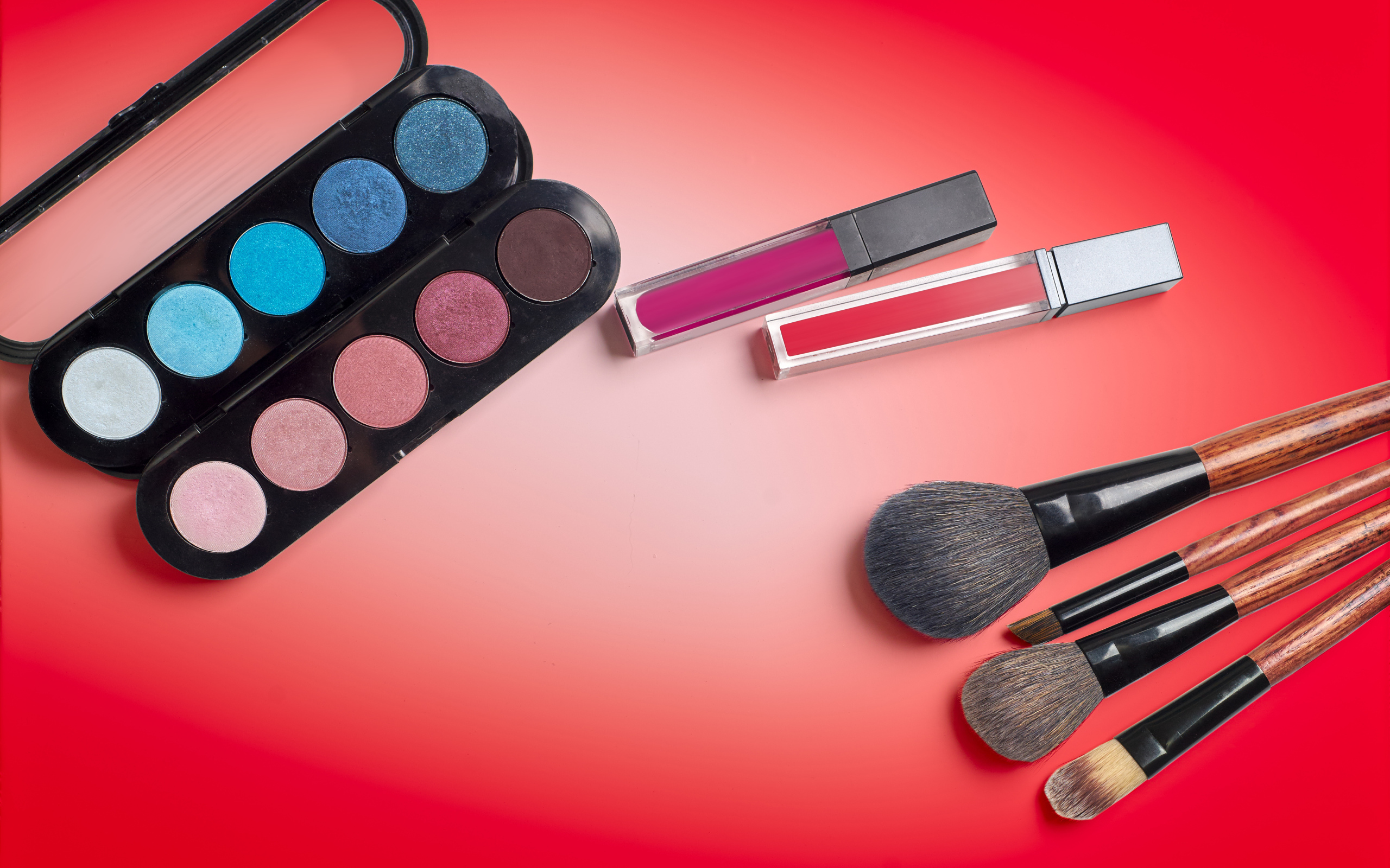 Блеск для губ, тени и кисточки на красном фоне