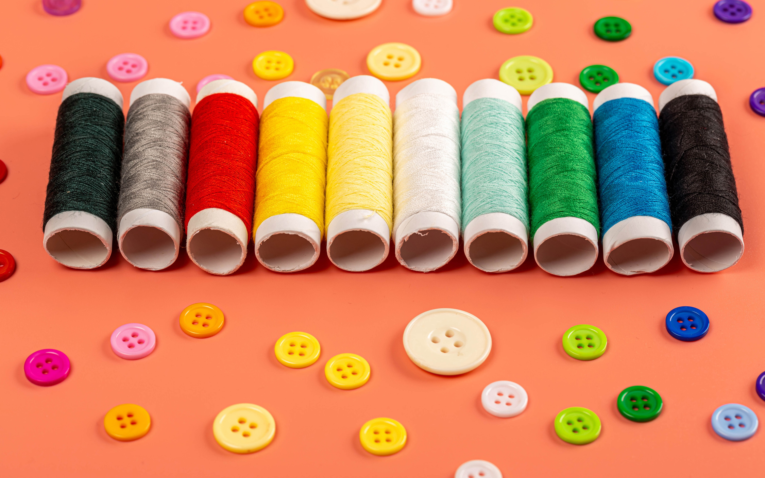 Разноцветные нитки и пуговицы на розовом фоне