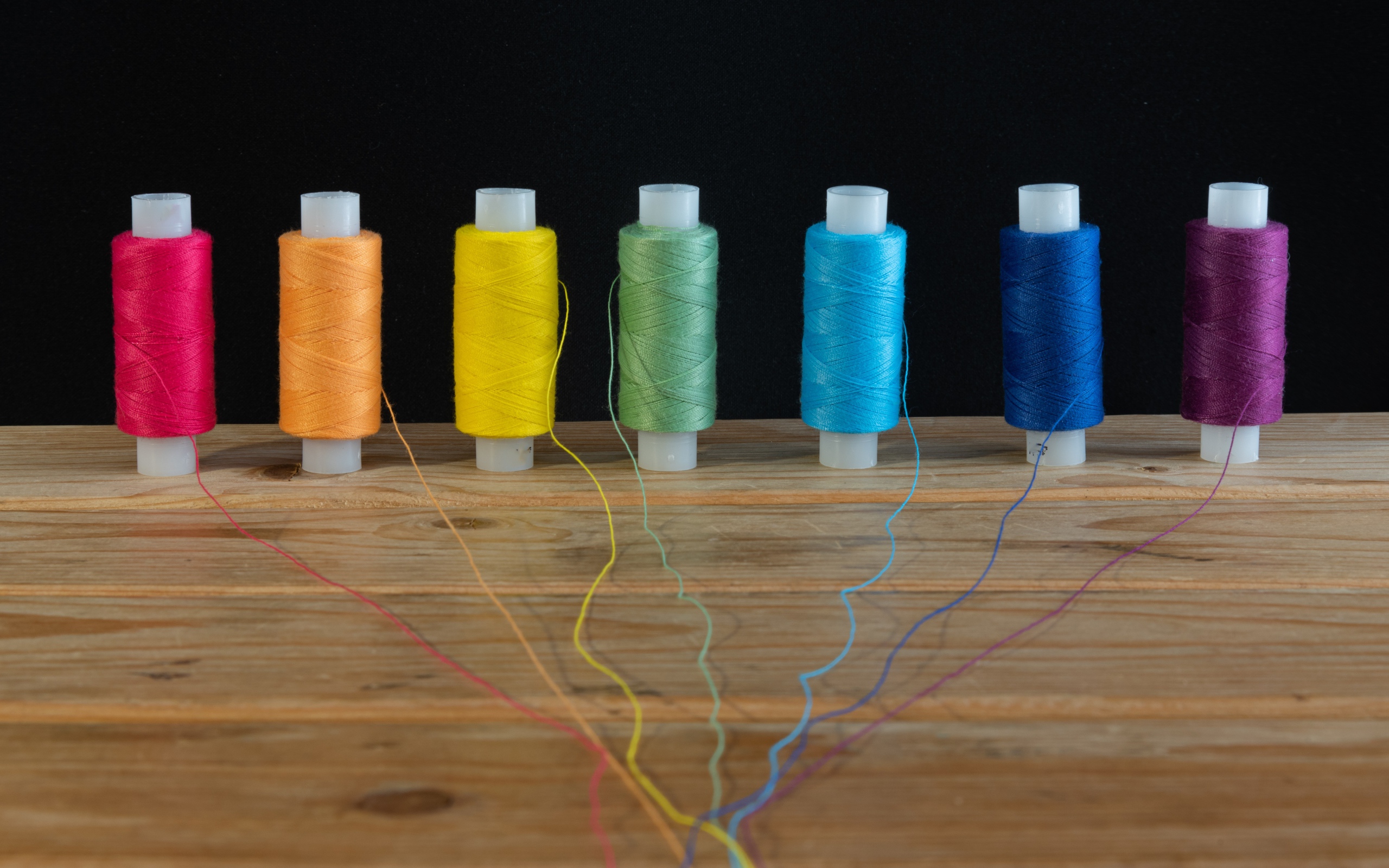 Катушки с разноцветными нитками на черном фоне 