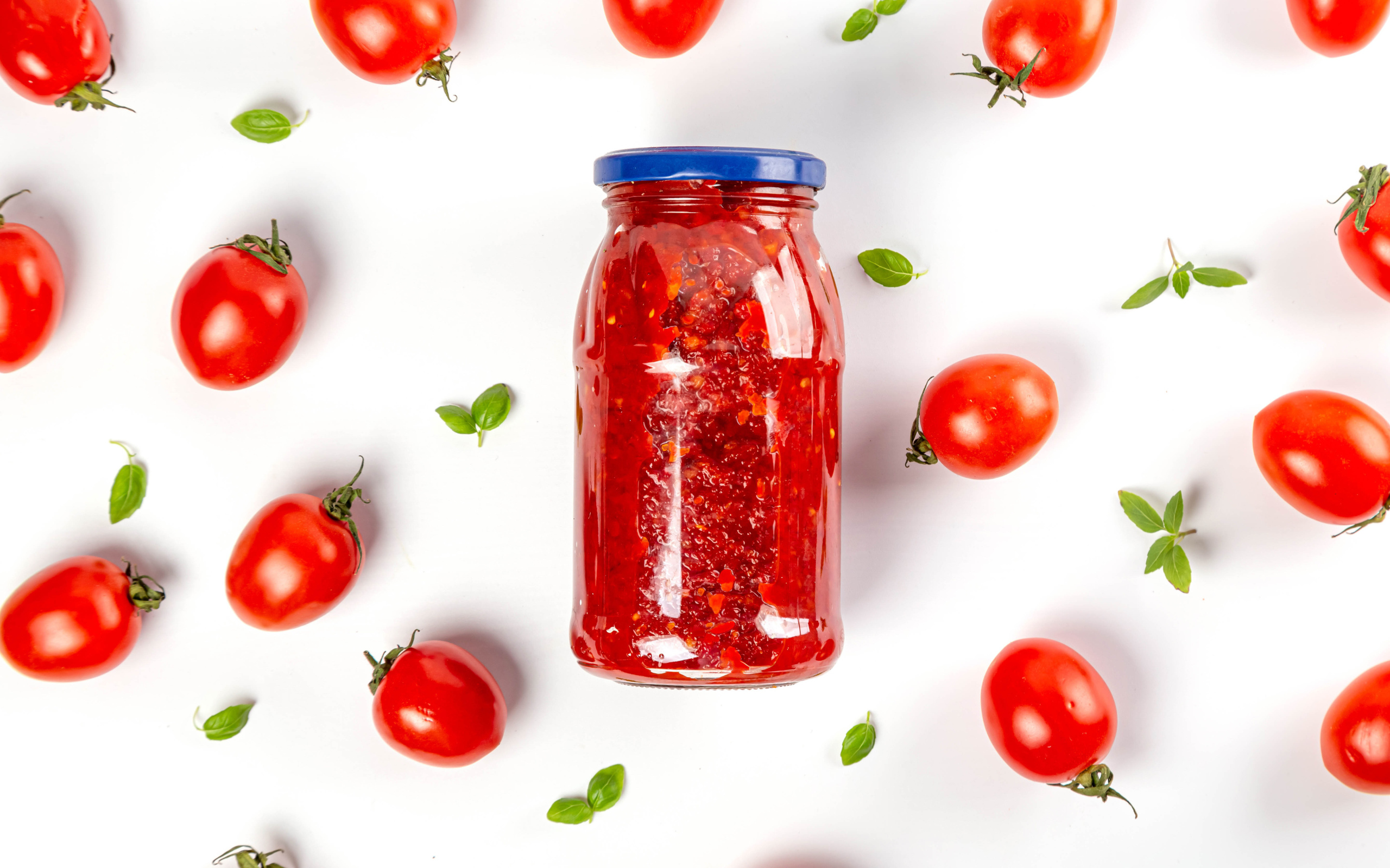 Банка аджики на белом фоне с помидорами