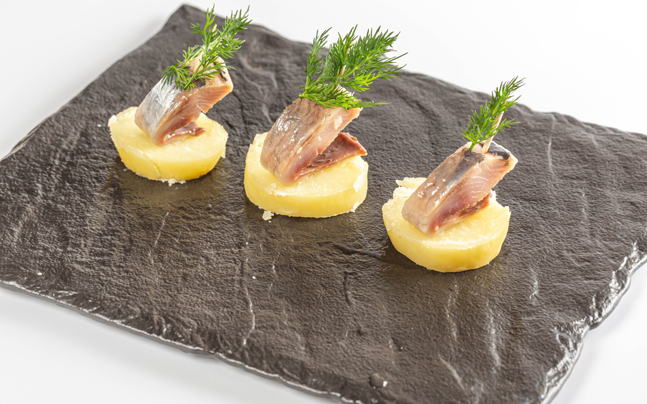 Три куска вареного картофеля с сельдью и укропом