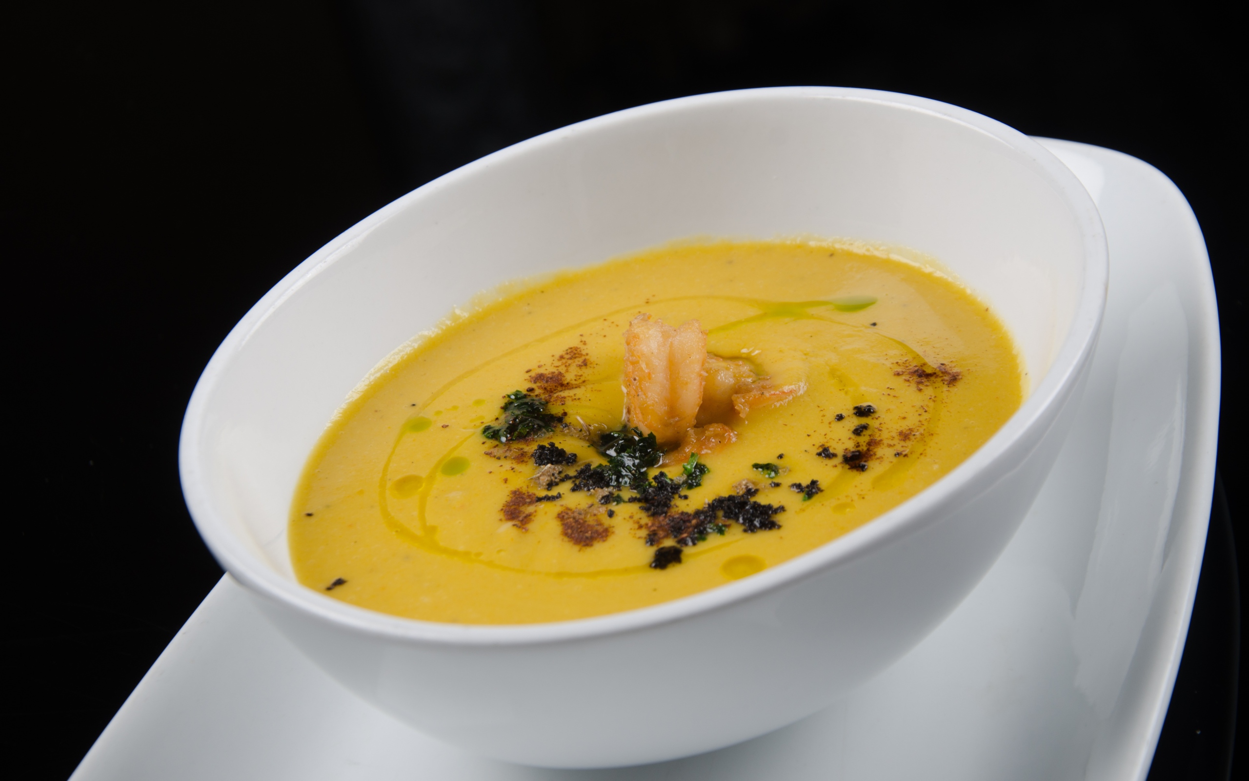 Желтый суп пюре в белой тарелке на черном фоне