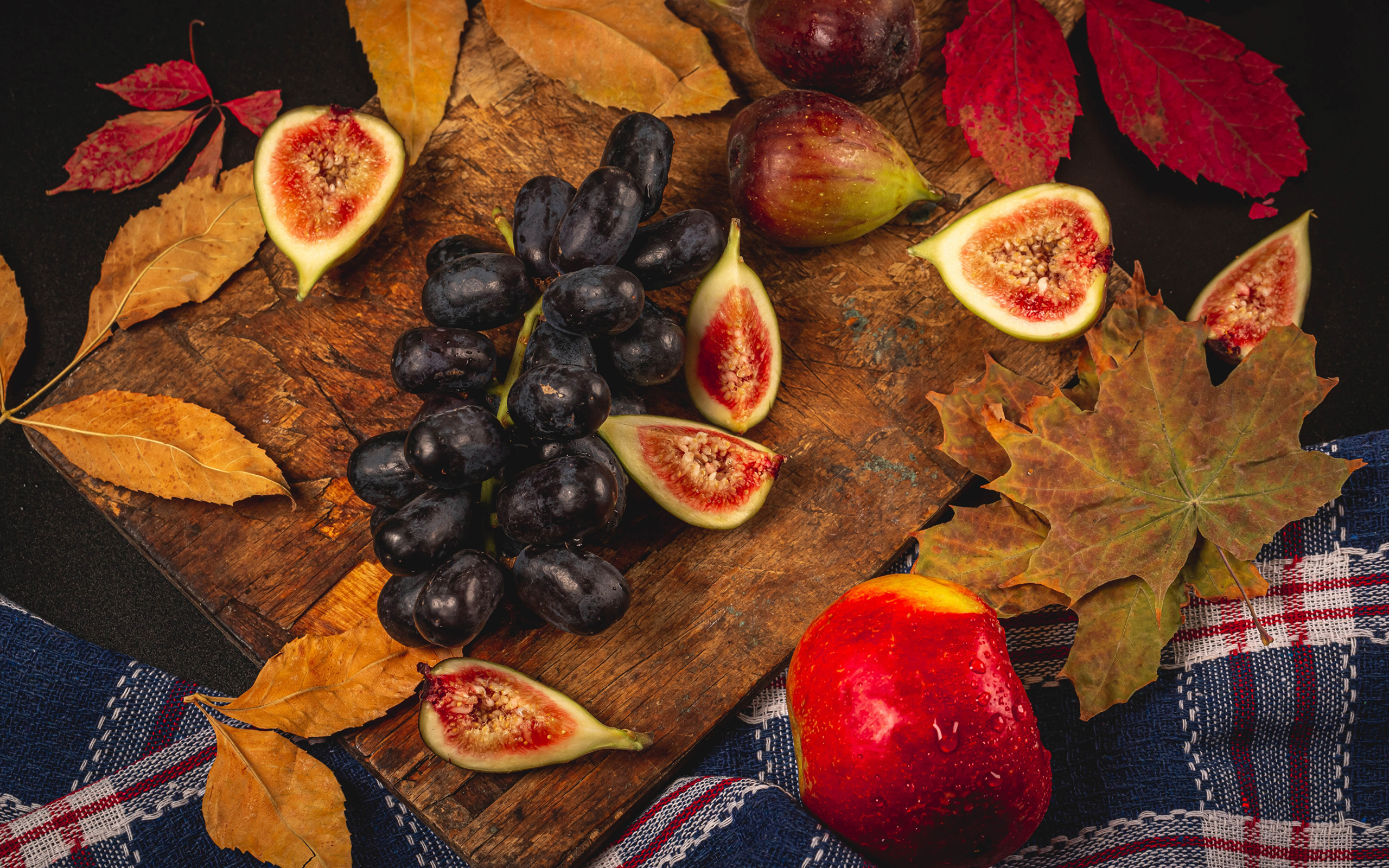 Синий виноград и плоды инжира на столе с листьями