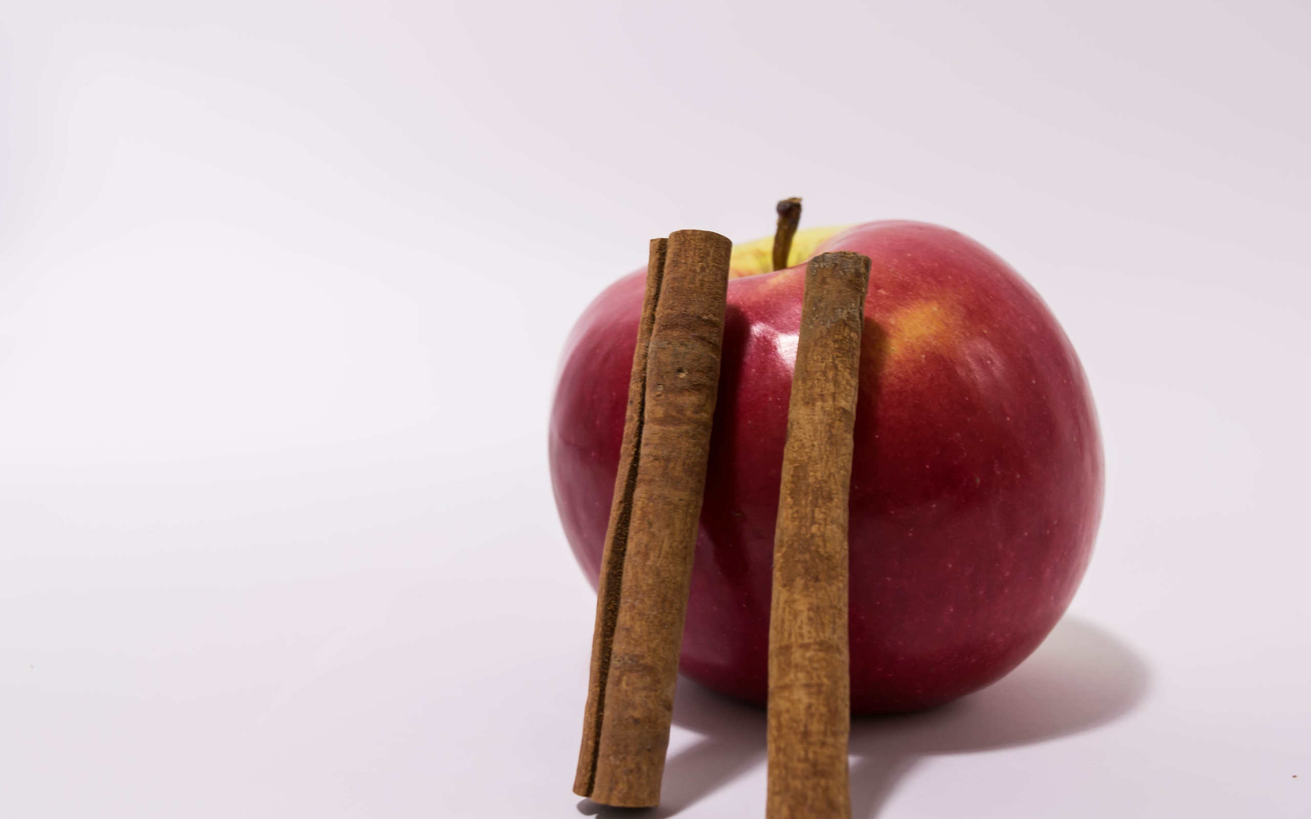 Красное яблоко с палочками корицы на сером фоне