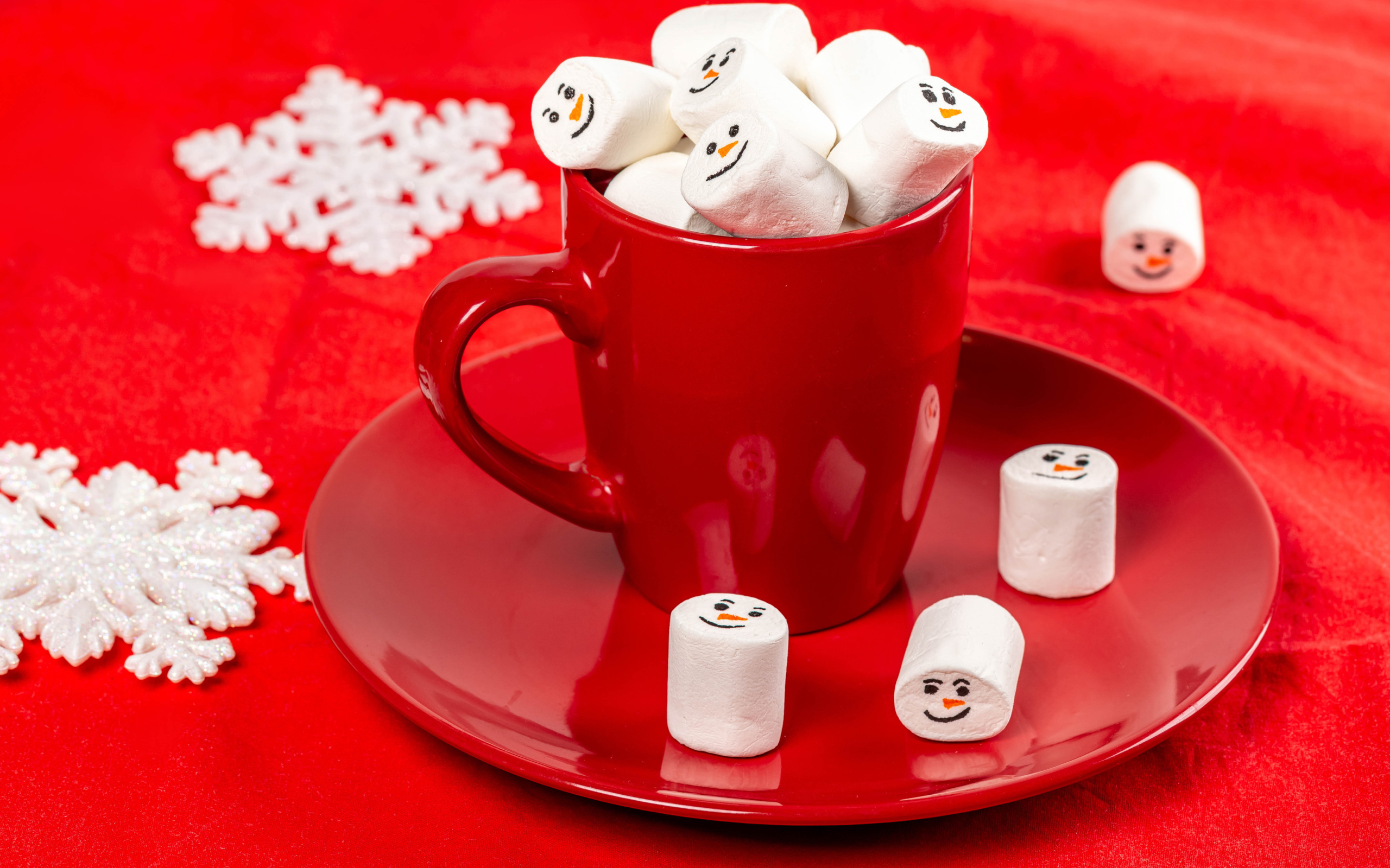 Красная чашка с маршмеллоу на столе со снежинками