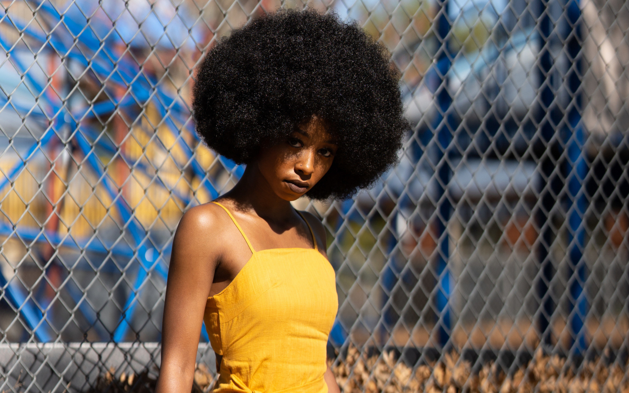 Темнокожая девушка в желтом платье стоит у сетки