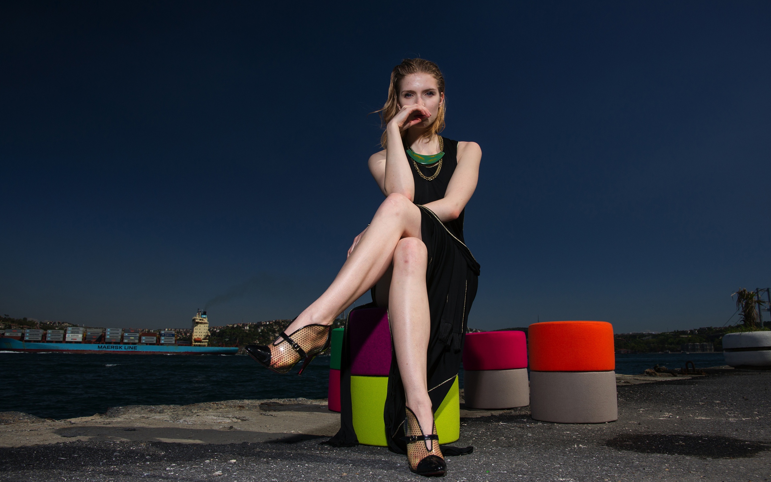 Девушка в черном платье сидит у воды