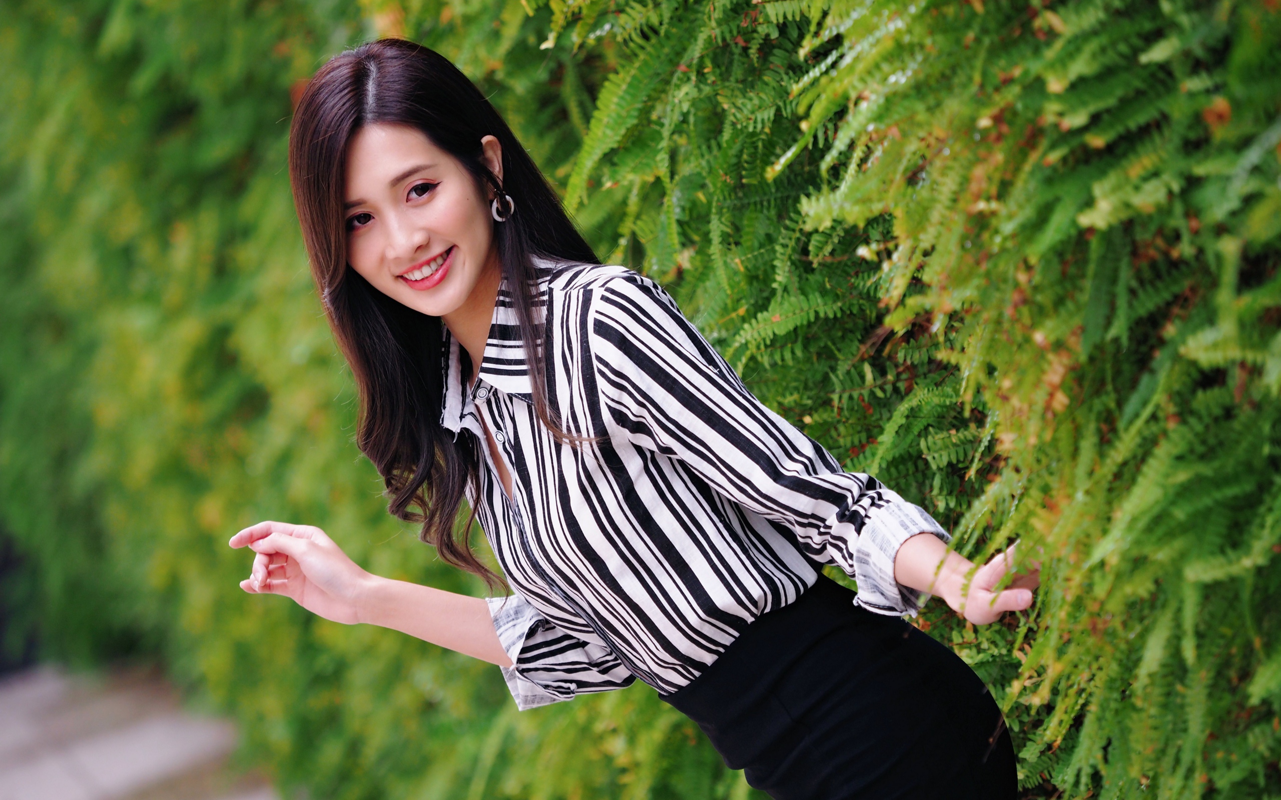 Красивая девушка в полосатой рубашке стоит у растения