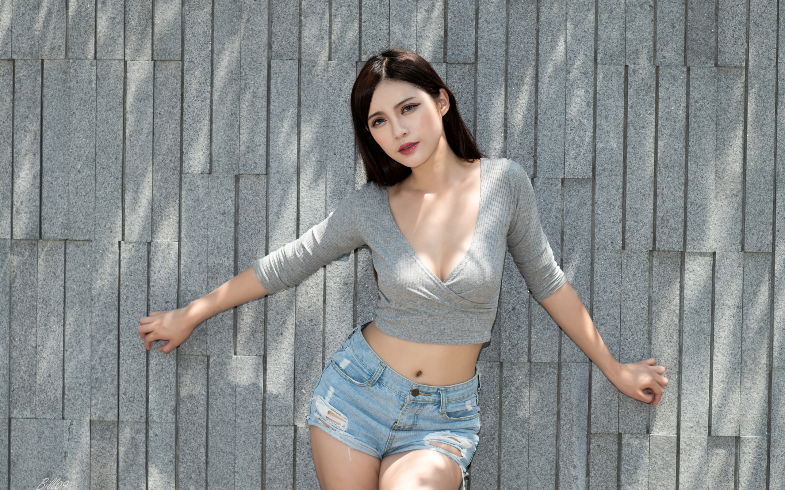 Милая девушка в серой кофте у стены 