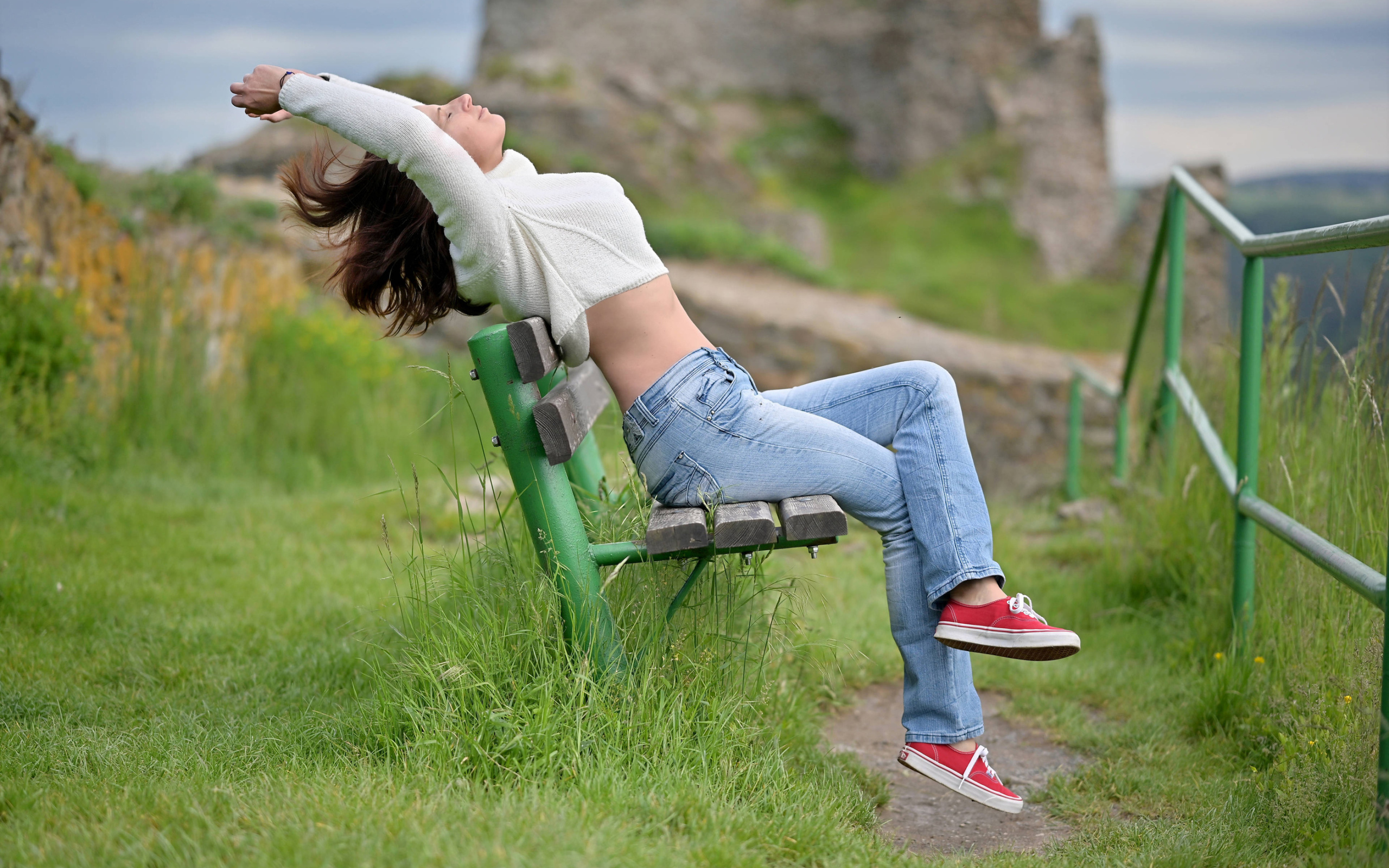 Девушка в синих джинсах сидит на лавке 