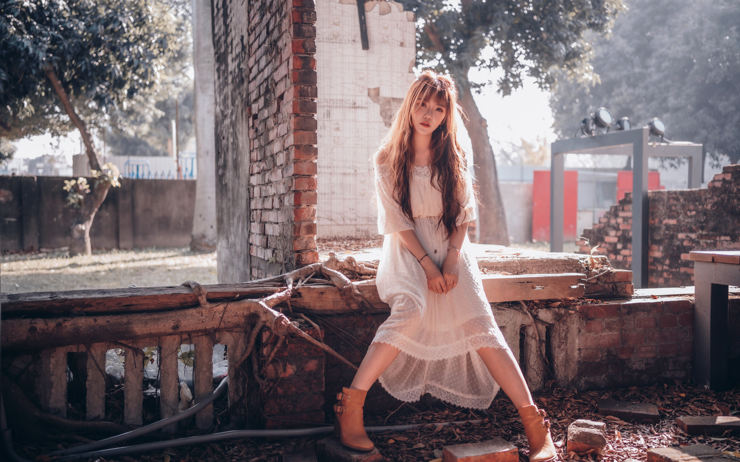 Молодая девушка азиатка в белом платье сидит на разваленной стене