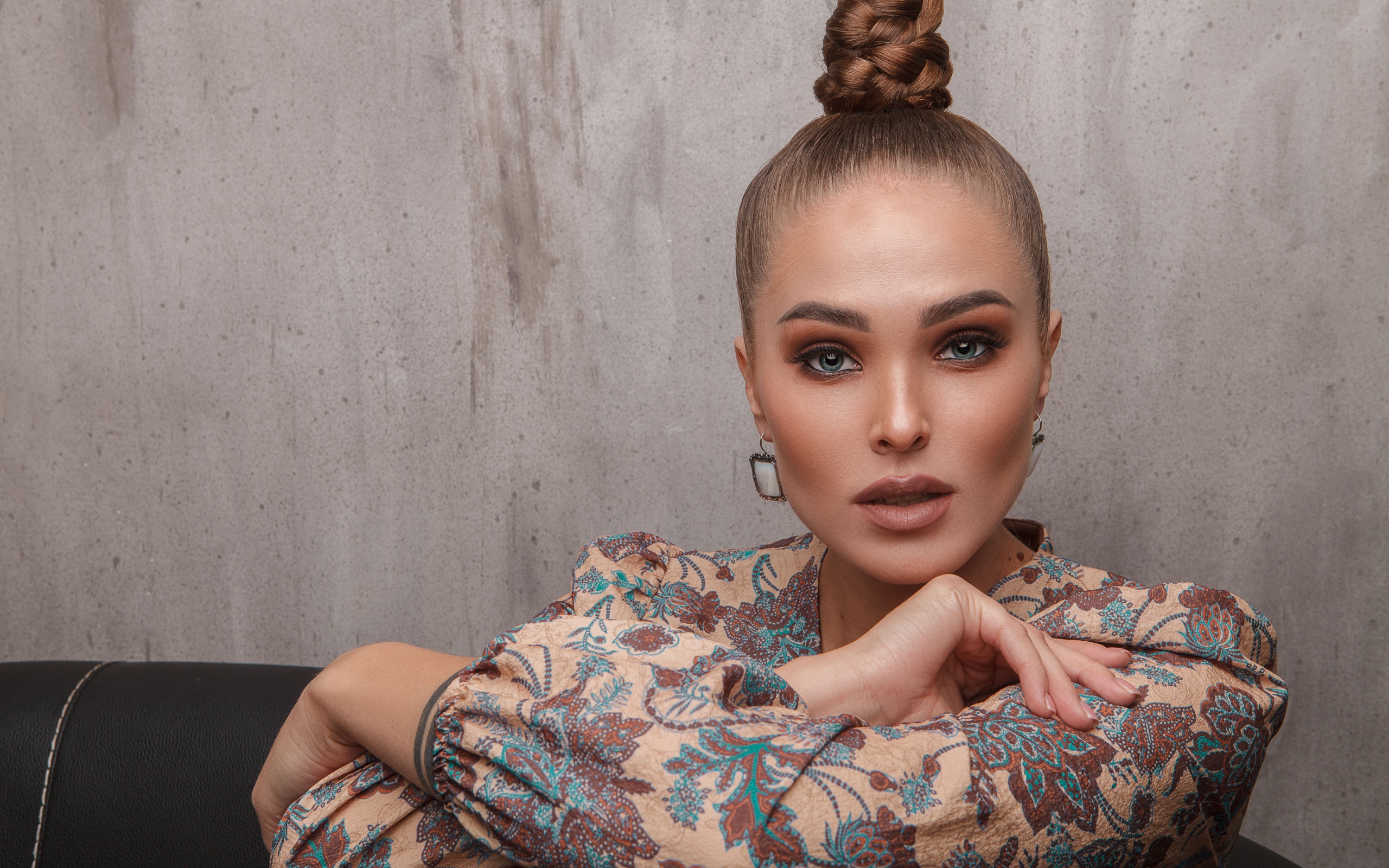 Молодая девушка с прической на голове на фоне стены